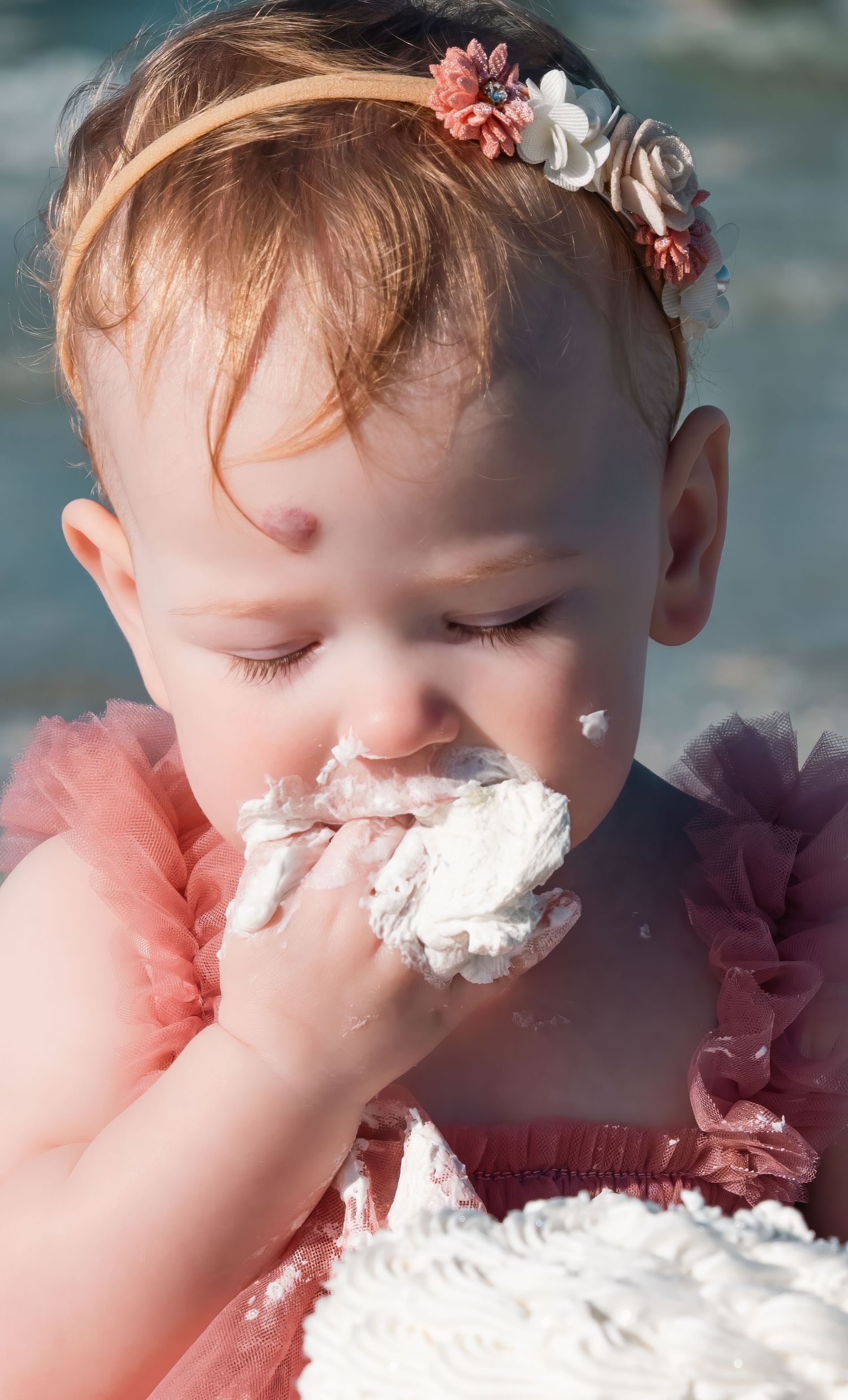 Baby girl in pink tutu eating first birthday cake smash outdoors.