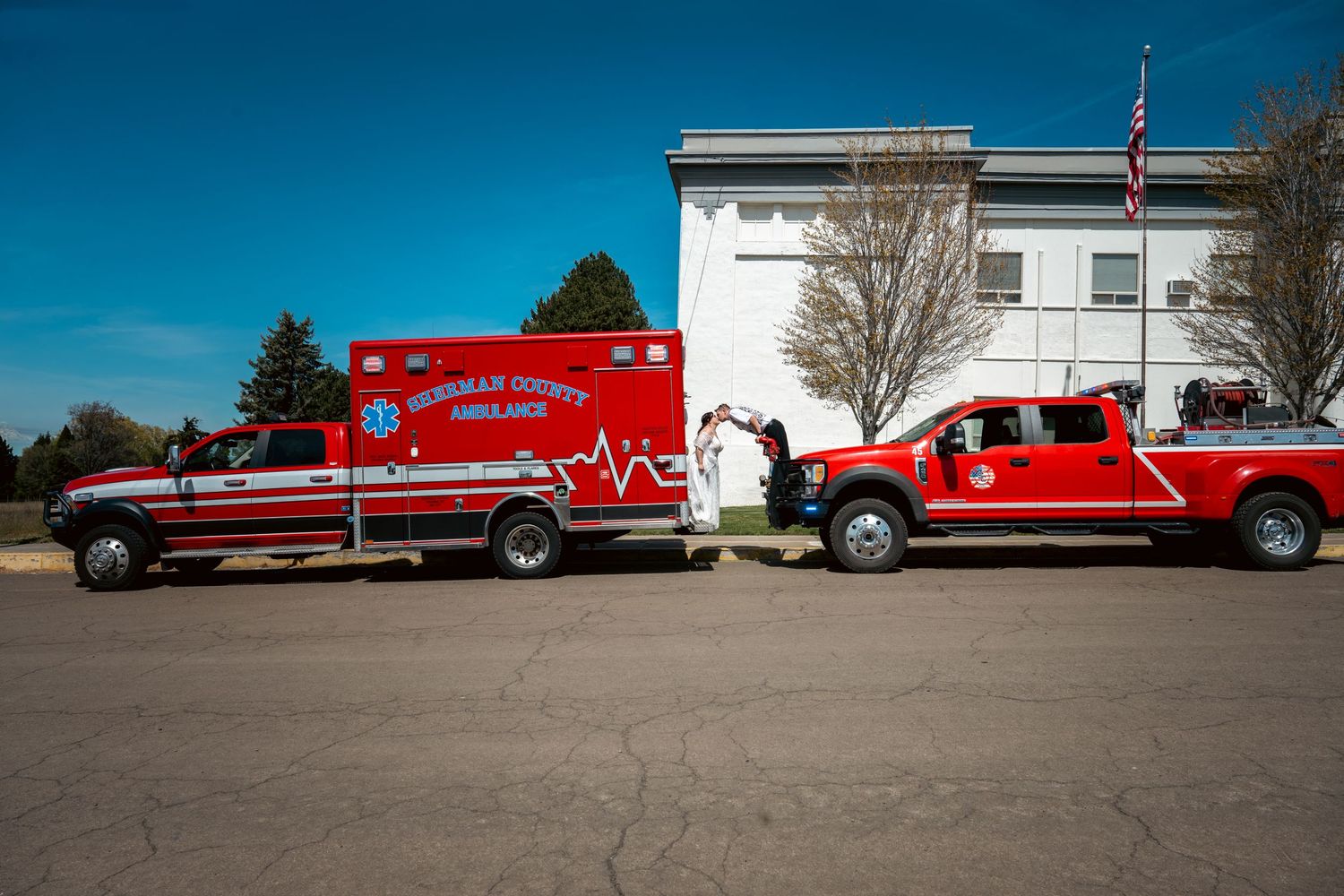 Sheridan County Ambulance and red fire truck parked outside a white building on a clear sunny day.