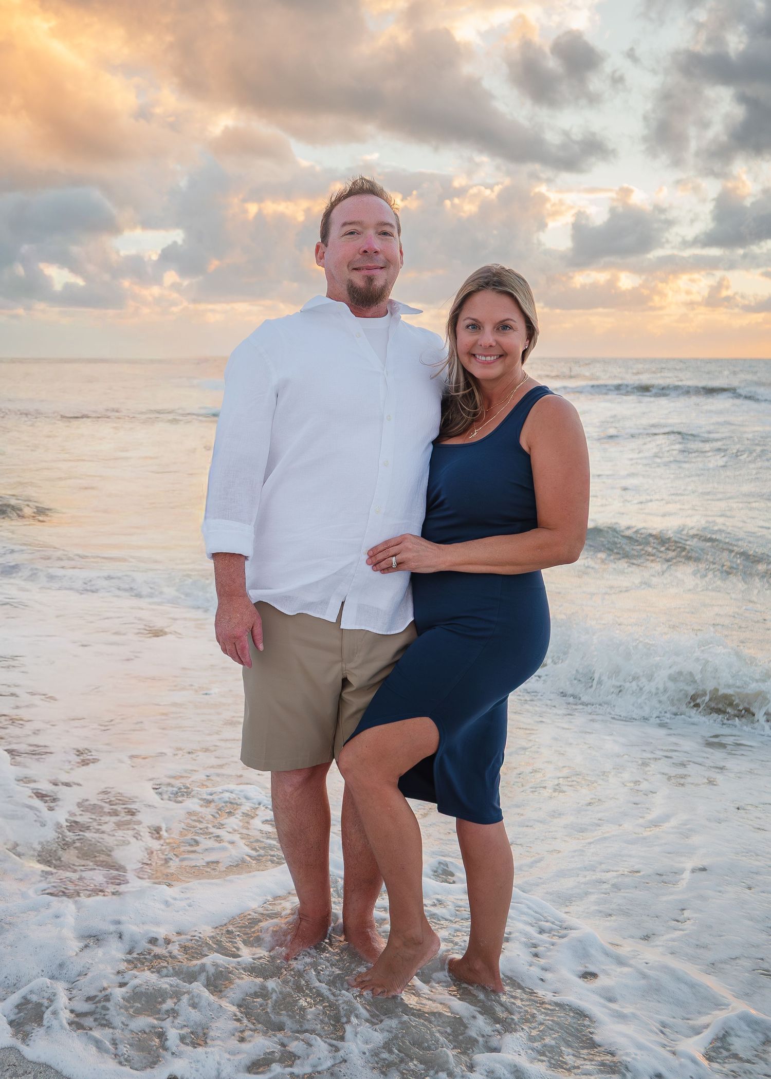 Couple posing together on beach at golden sunset with waves behind them.