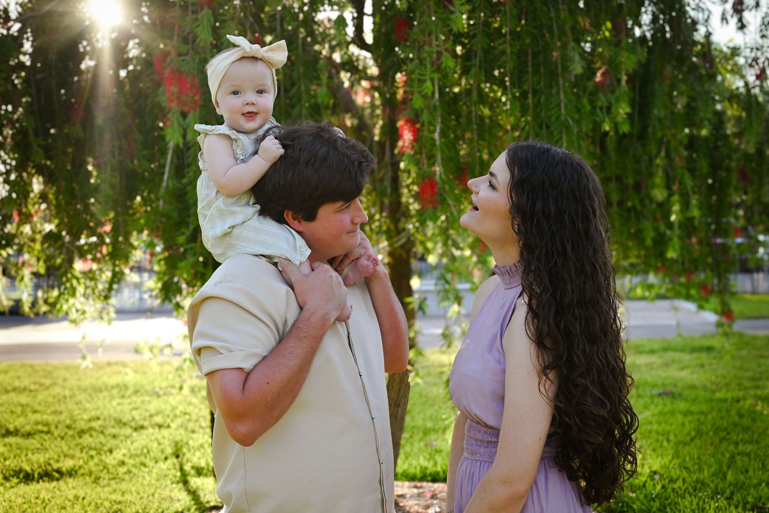 A young family with a baby enjoys a sunny day in a lush green park.