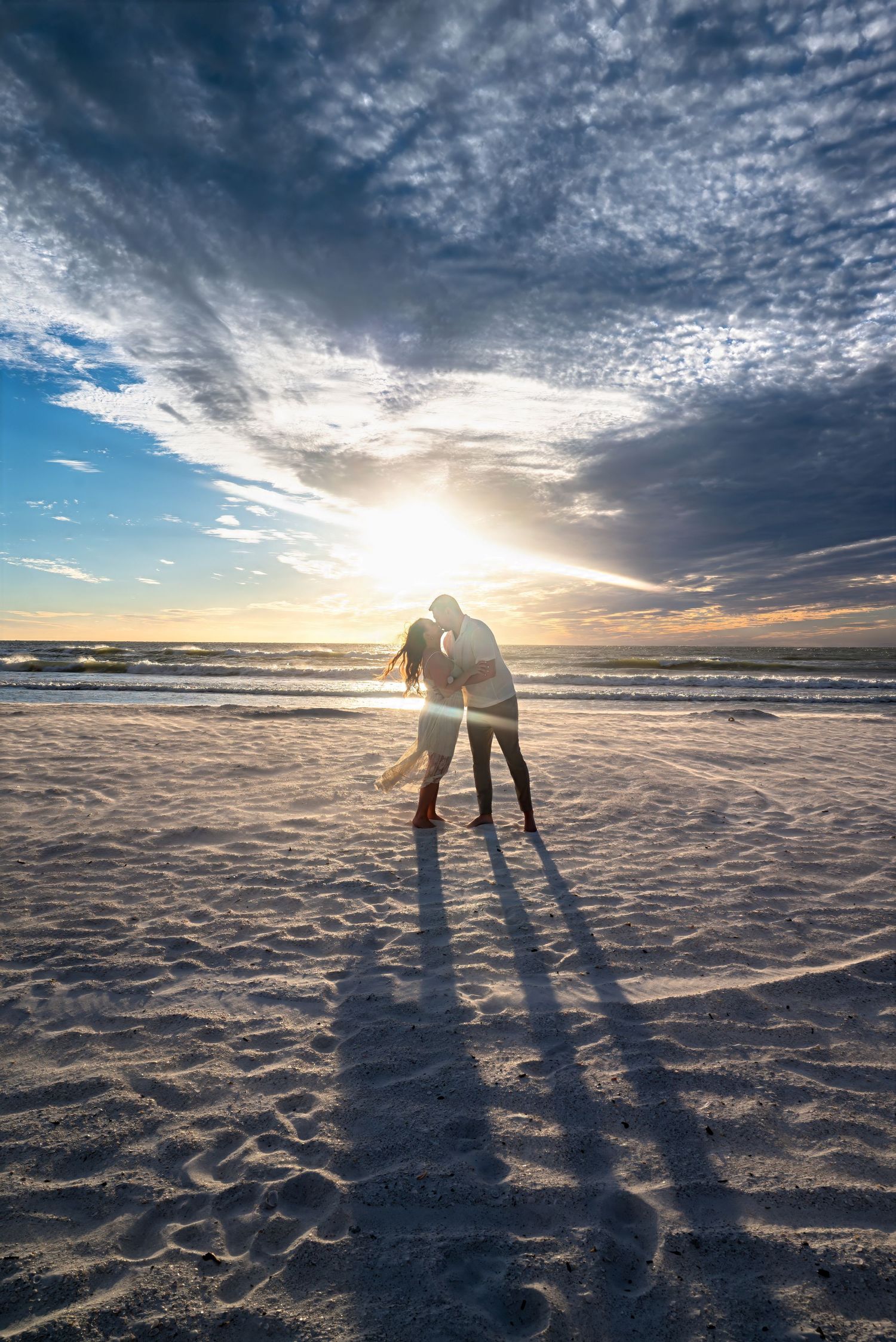 Couple kissing in dramatic sunset light on sandy beach.