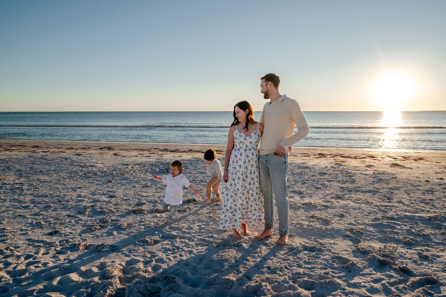 Young family with two toddlers enjoying golden hour on sandy beach.