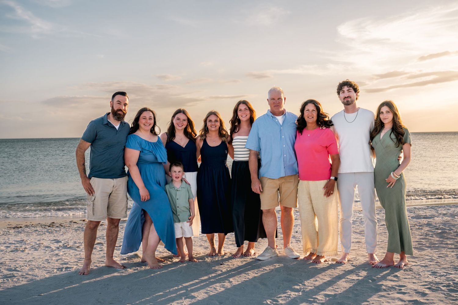 Family group photo on a sandy beach at sunset, smiling and posing together near the ocean shoreline.
