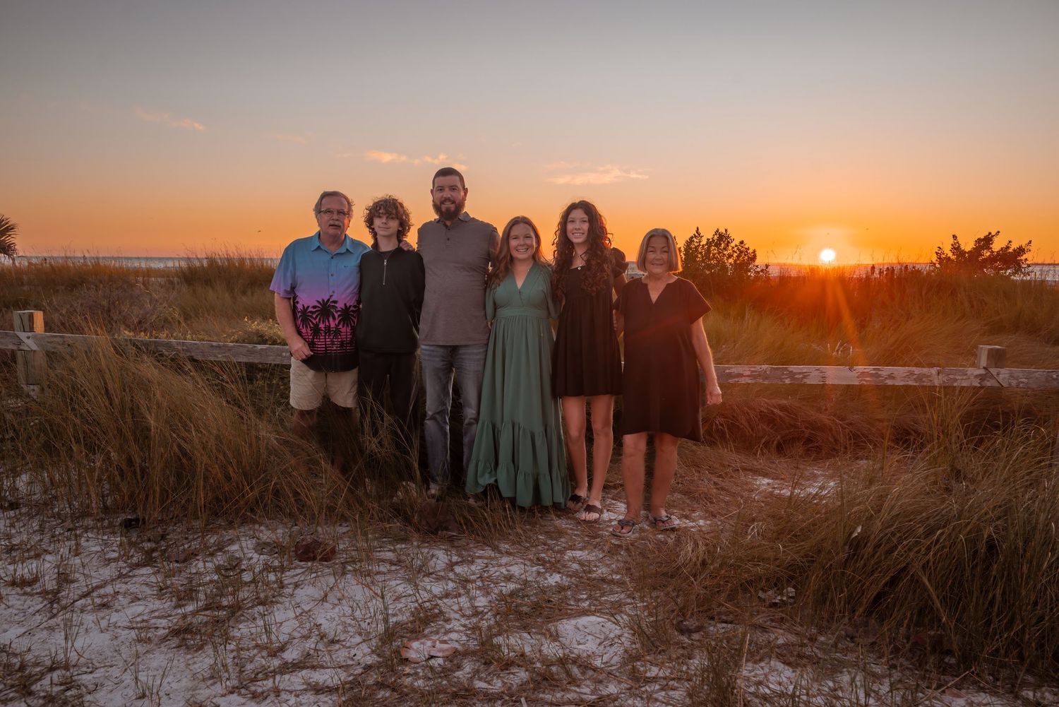 A family of six poses together at sunset on a sandy beach path.