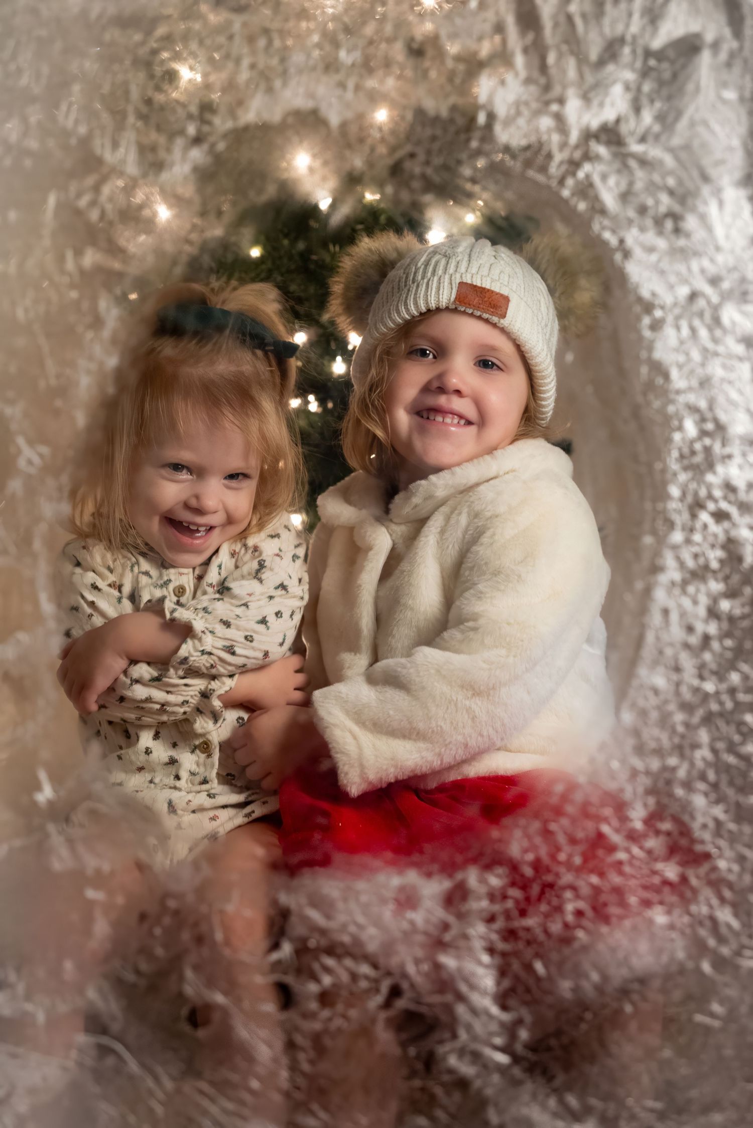 Two smiling young girls pose in a festive winter Christmas photo setup with twinkling lights and snowy decor in Southwest Florida