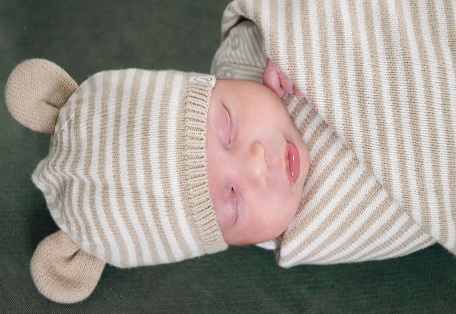 Peaceful newborn baby sleeping in striped beige and white swaddle with bear ear hat.