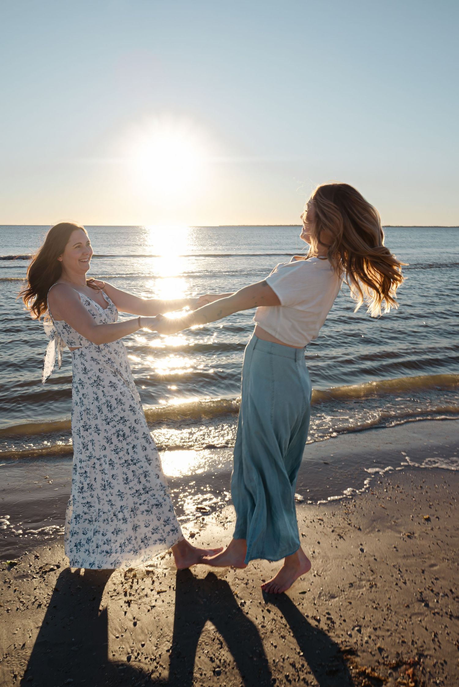 Two women dancing and spinning together on sunny beach at sunset.