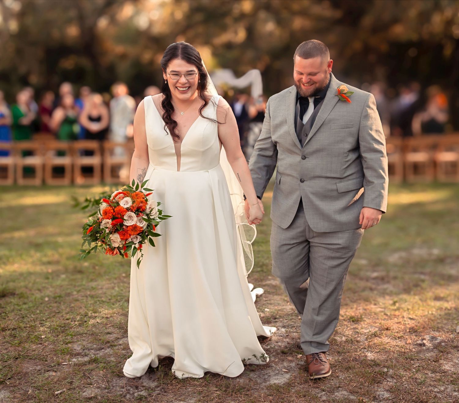 Happy newlyweds walk down the aisle hand in hand after outdoor wedding ceremony.