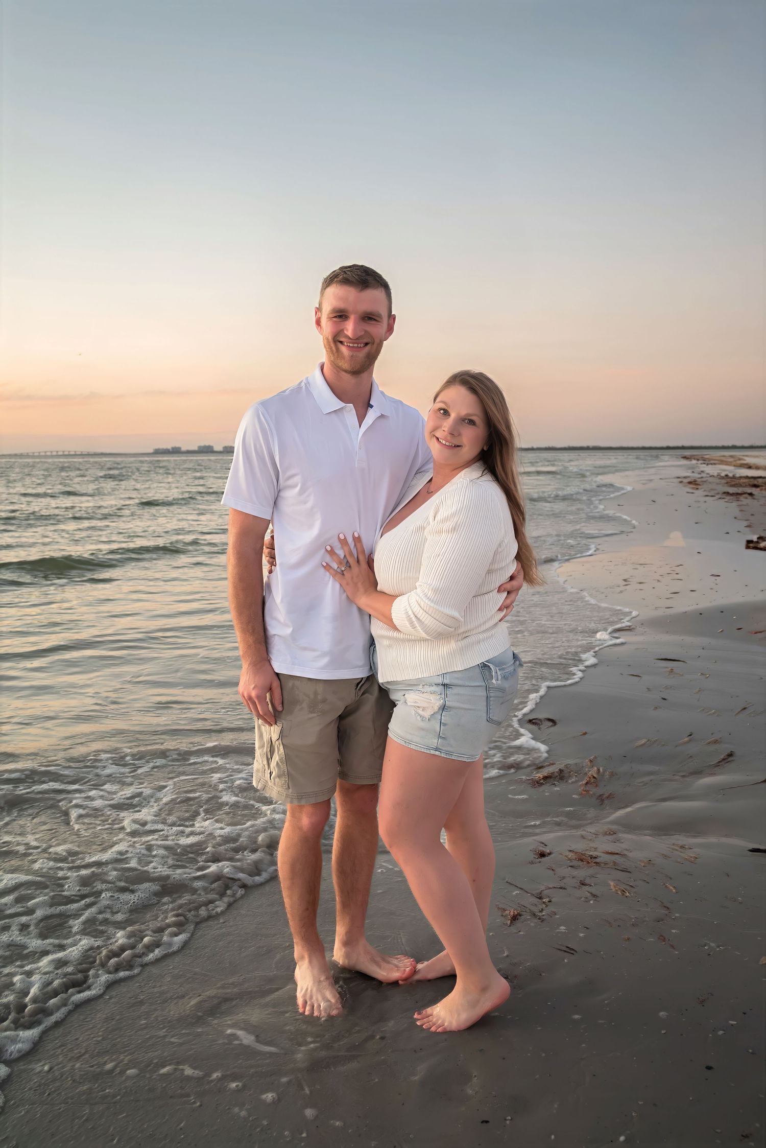 Smiling couple embracing on sandy beach at colorful sunset by the ocean.
