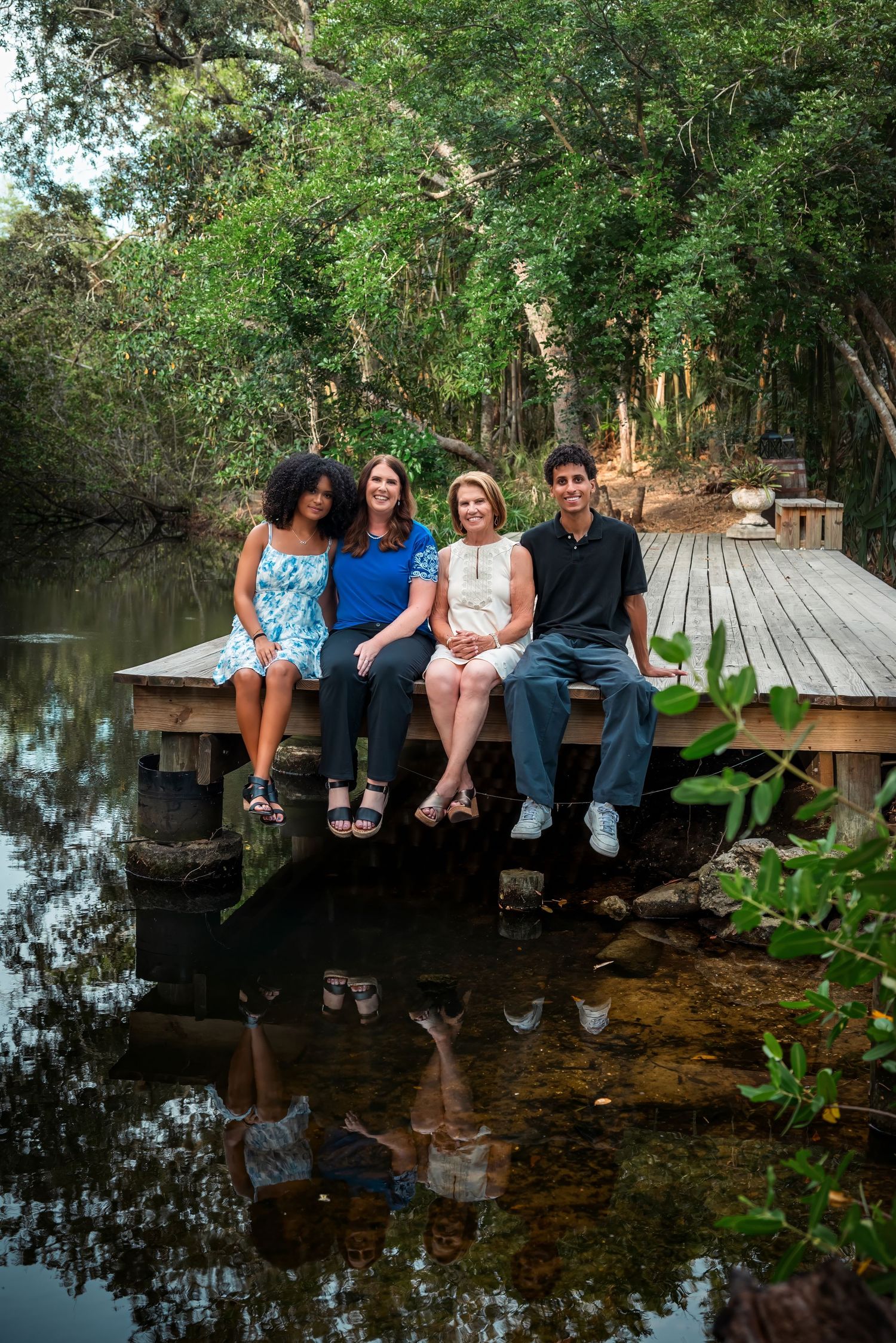 Four people sitting on a wooden dock over a calm river surrounded by lush green trees, smiling for a family portrait.