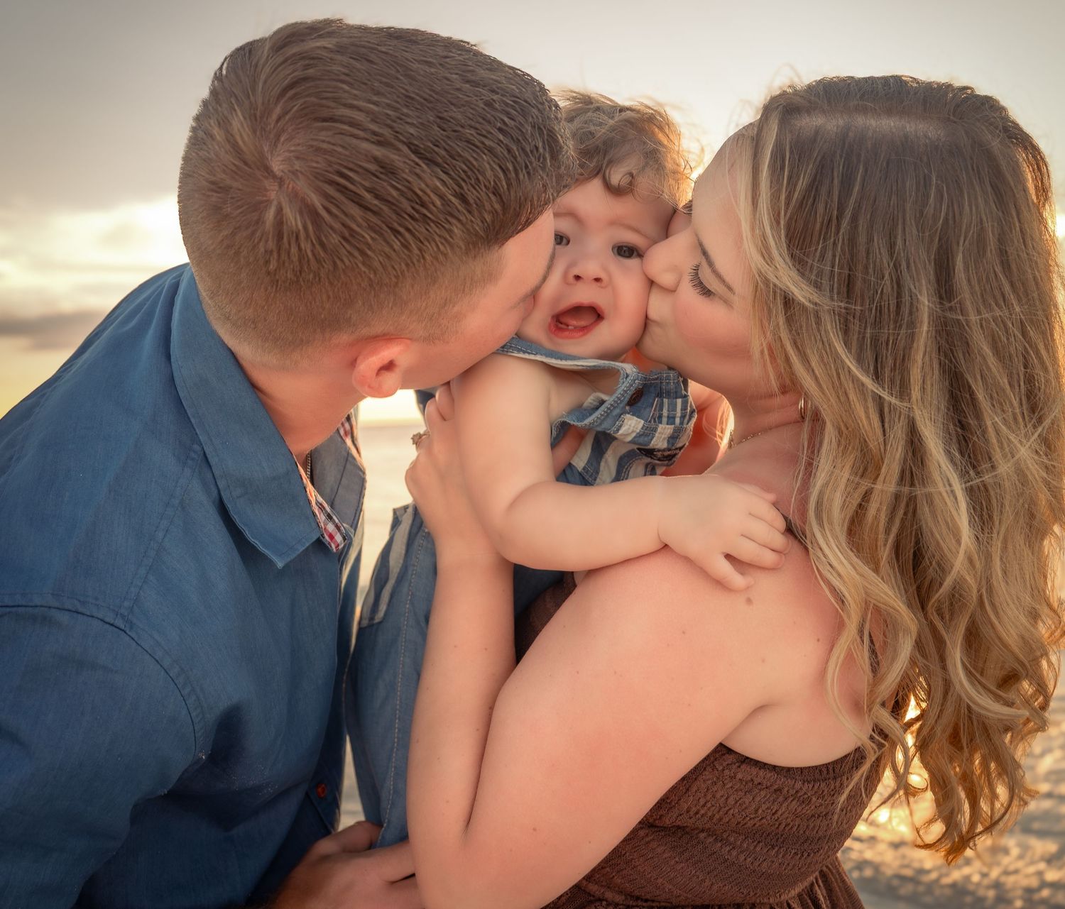 Loving parents kissing their happy baby on the cheeks during a golden hour beach photo session.
