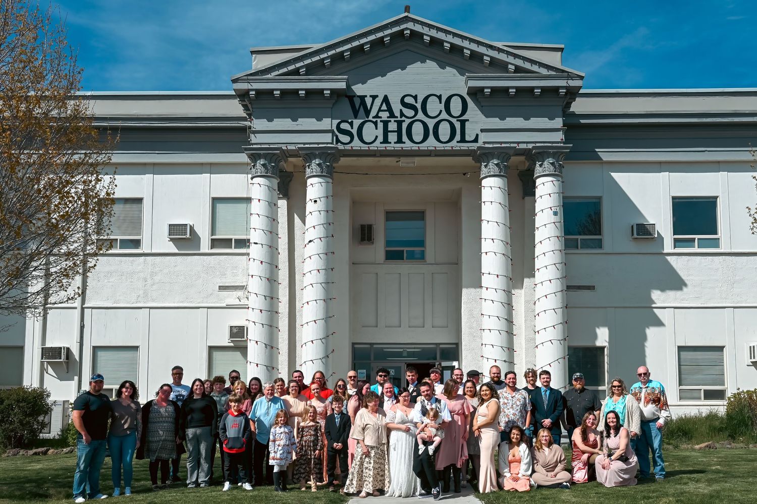 Large group of people posing in front of Wasco School, a classic white building with tall columns on a sunny day.
