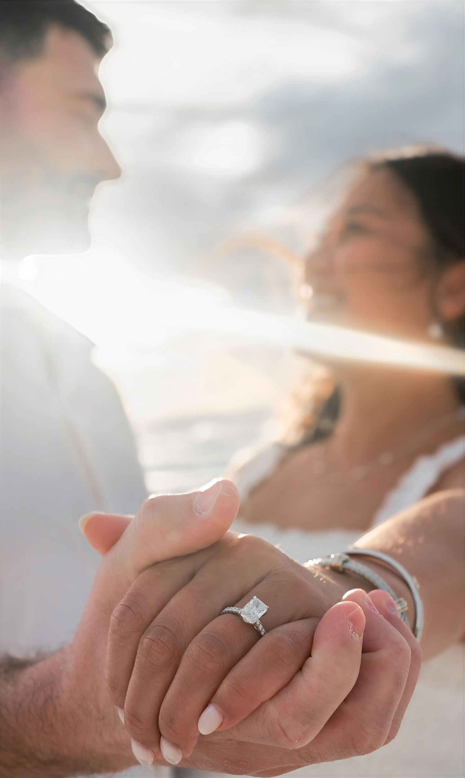 Close-up of engagement ring on couple holding hands at beach.