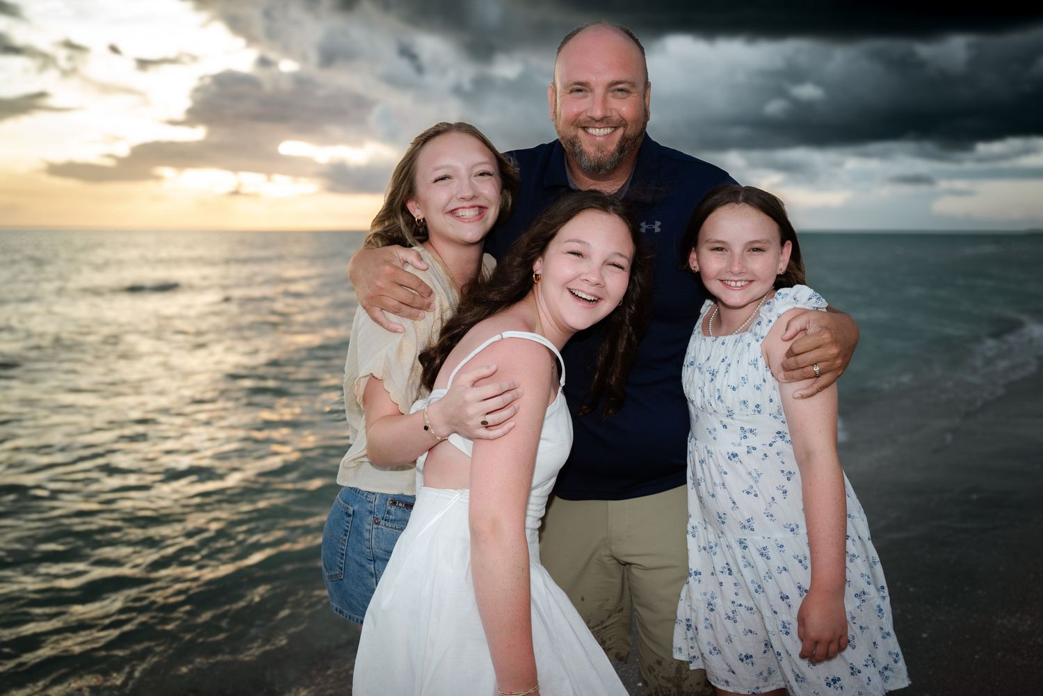 Father hugging three daughters at sunset on the beach.