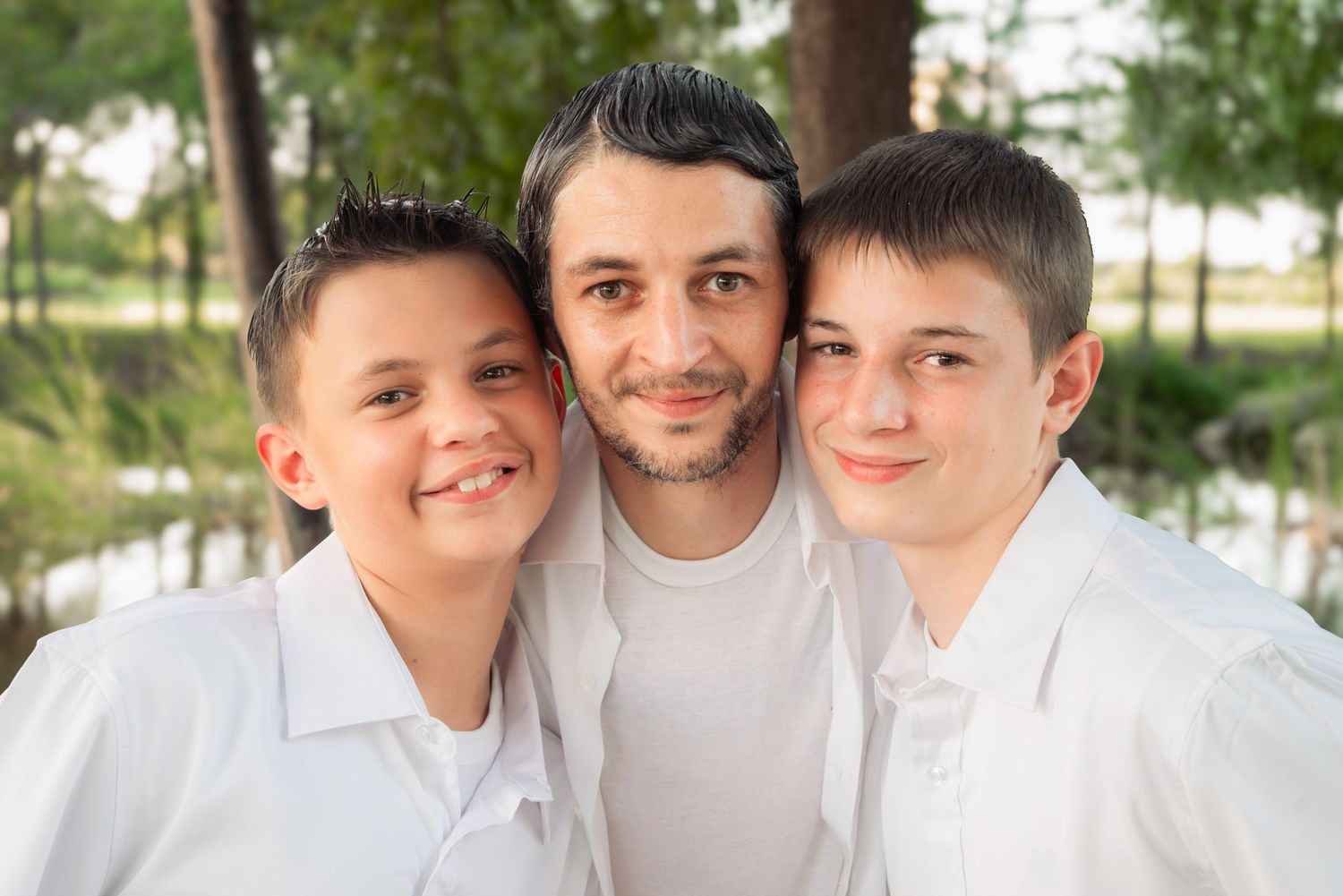 A man smiles with two boys in white shirts outdoors.