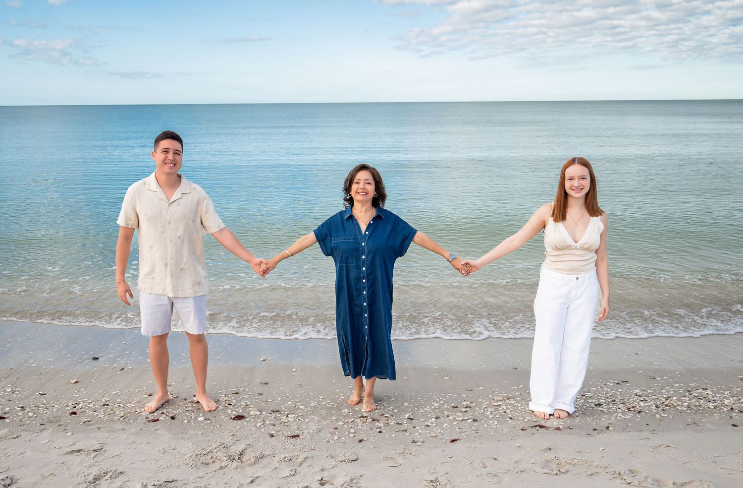 Three family members holding hands on a beach with ocean behind them.