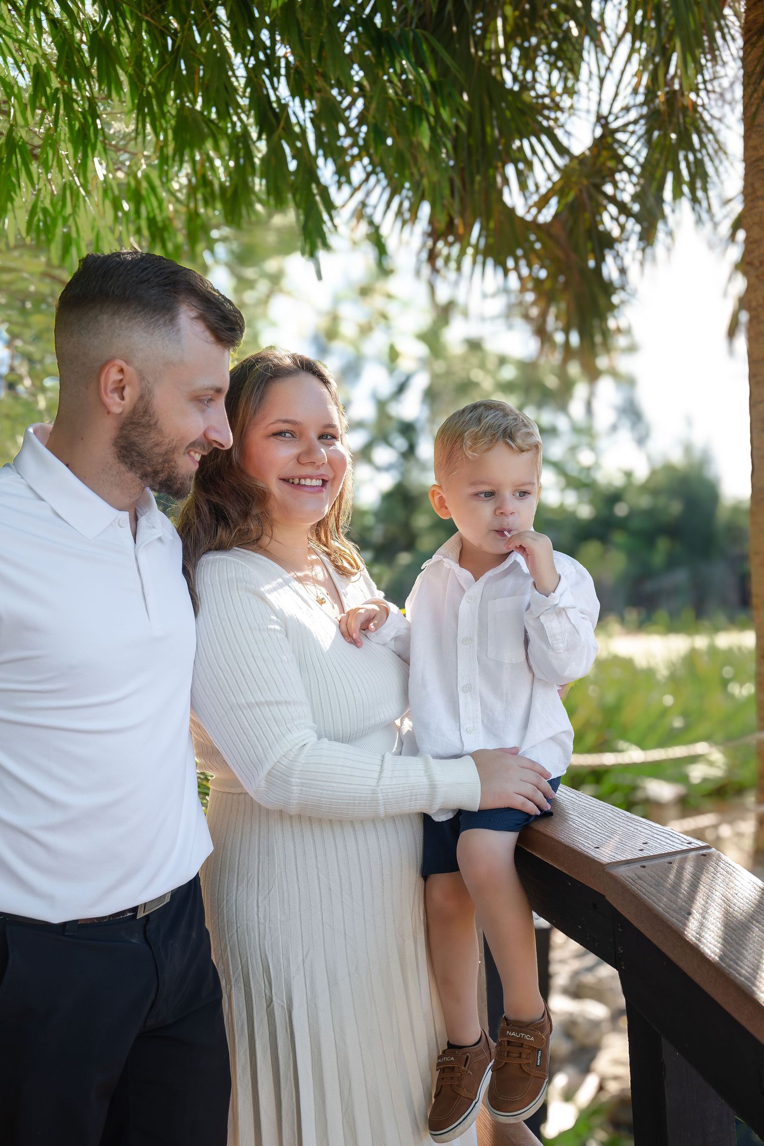 Smiling family with young boy standing on a wooden deck surrounded by lush tropical palm trees.