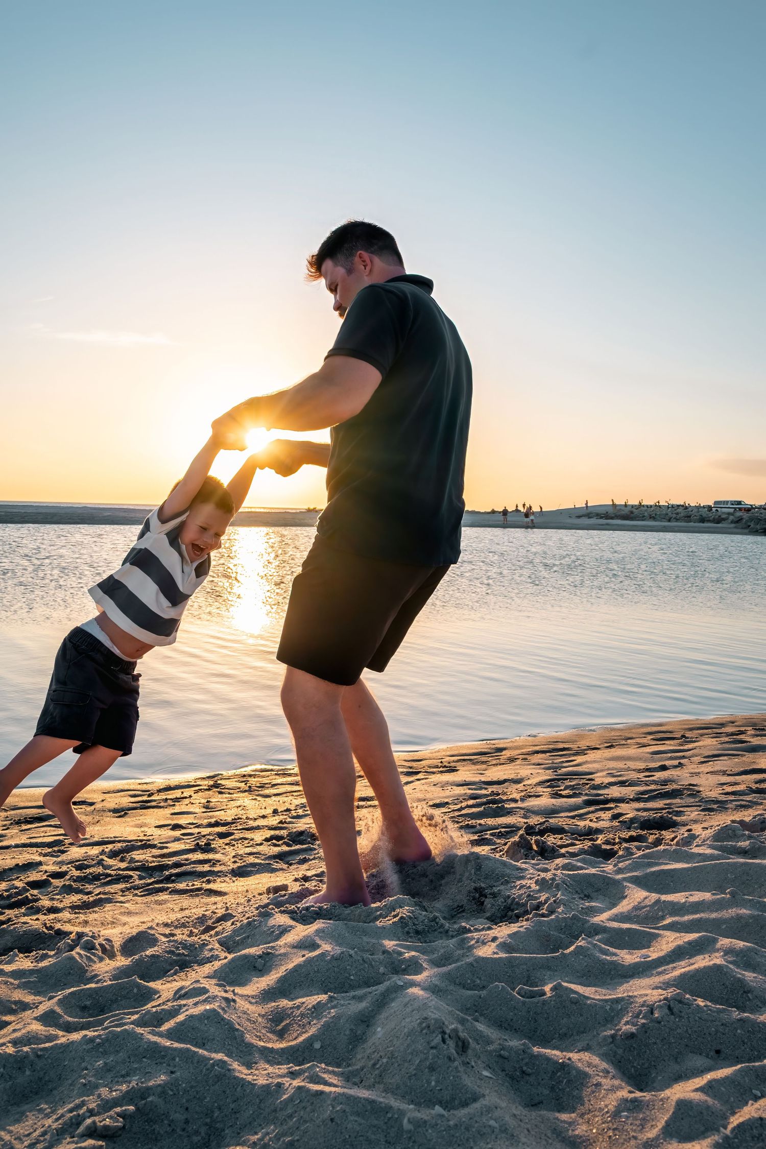 Father and child playing on sandy beach at golden sunset by the water's edge.