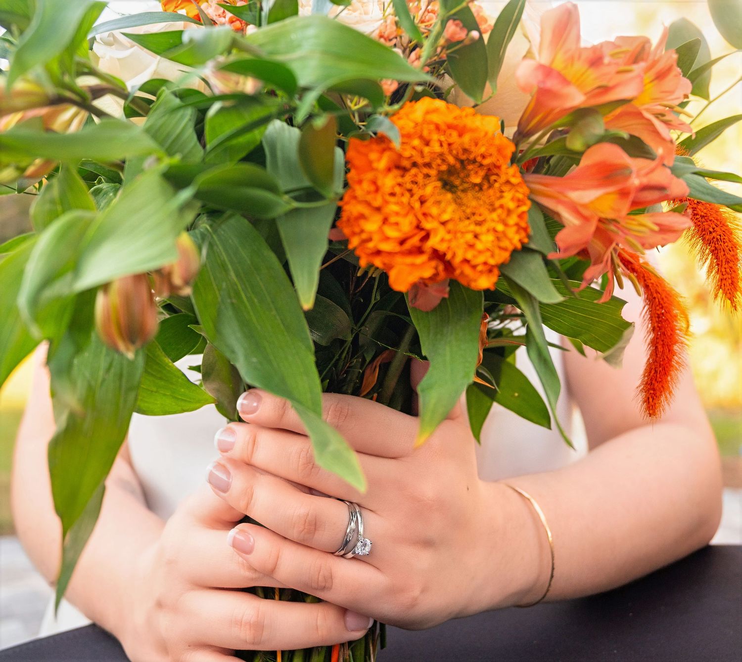 Close-up of bride holding a vibrant orange and green wedding bouquet, wearing a silver ring.