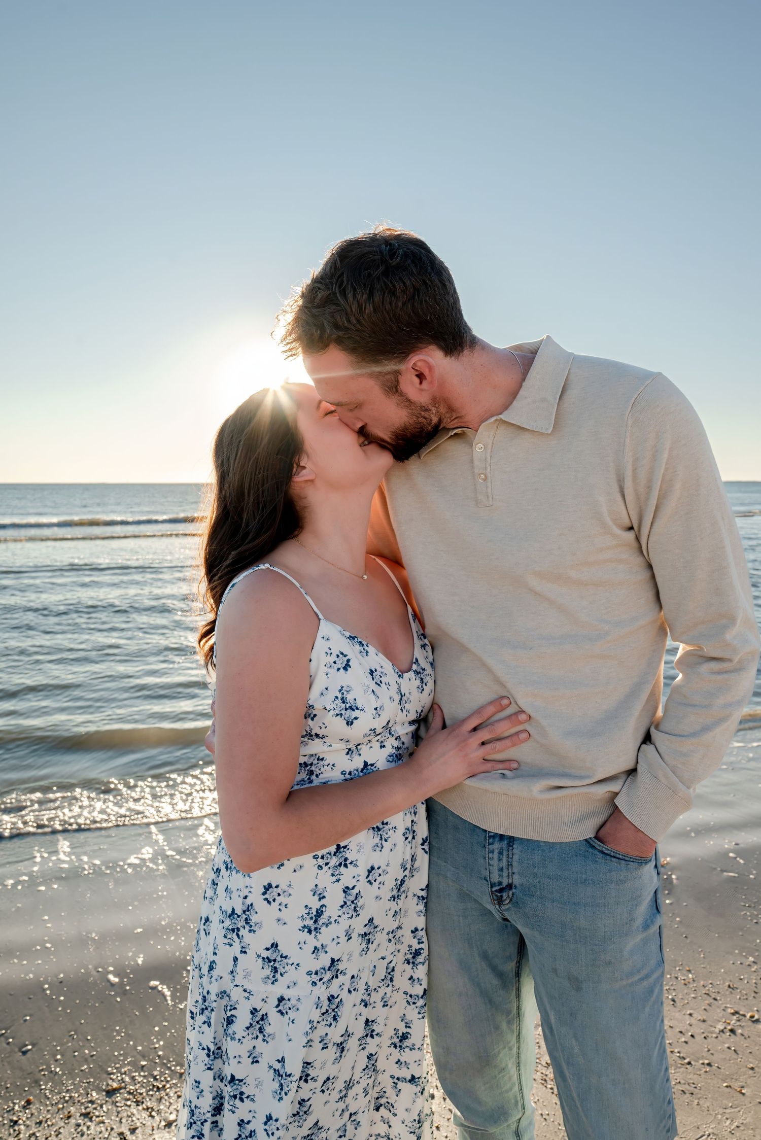 Young couple kissing on a sunny beach, the woman wearing a floral sundress.