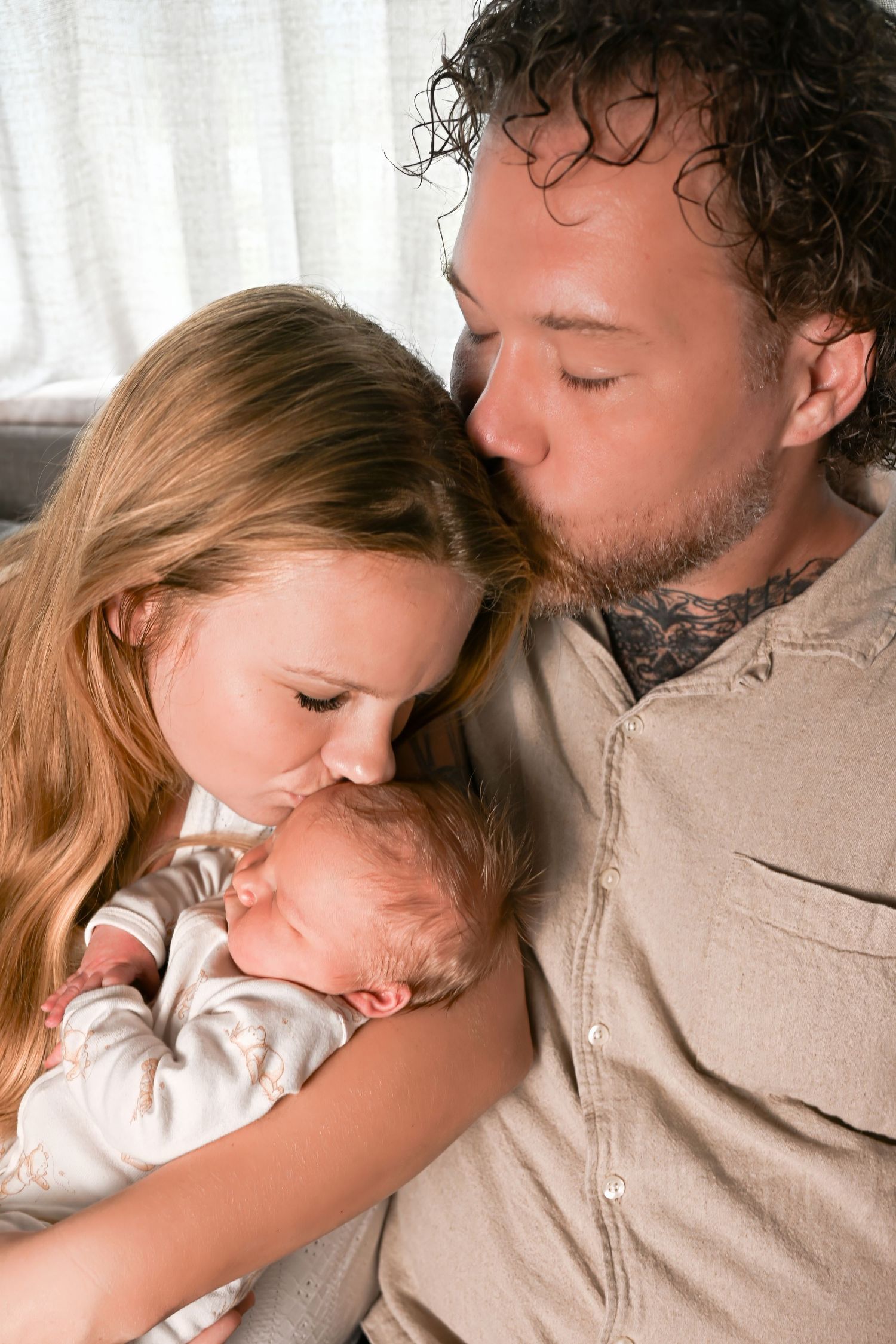 New parents tenderly kissing their sleeping newborn baby together, sharing a loving family moment.