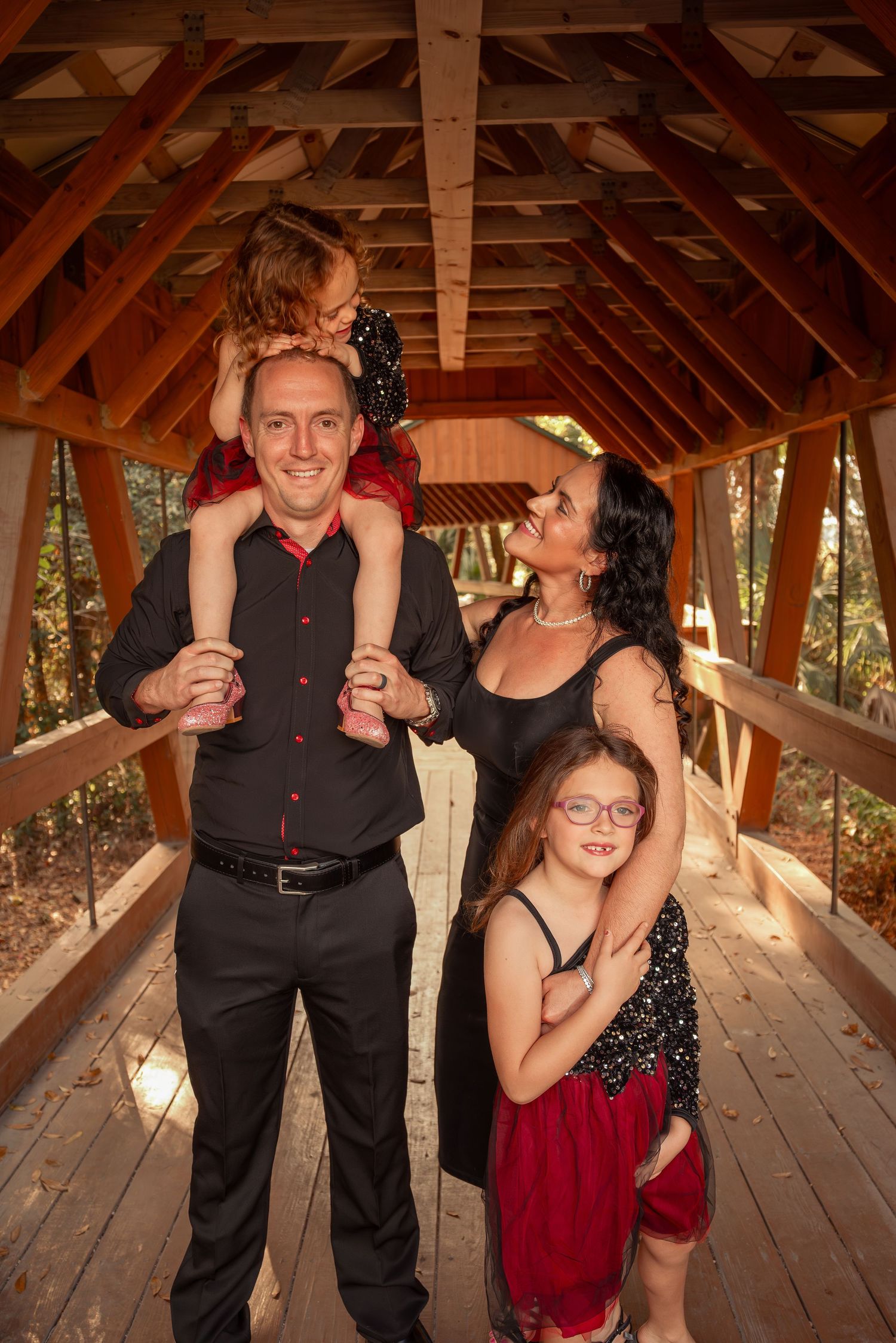 Joyful family of four laughing together inside a rustic wooden covered bridge during a photo session.