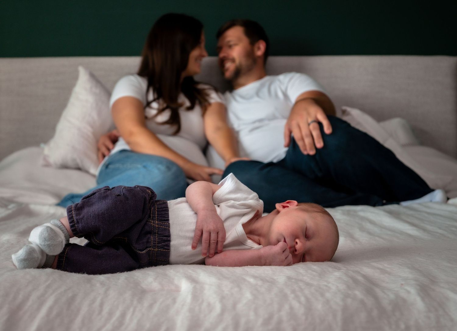 Couple relaxing on bed smiling at each other while newborn baby lies in foreground.