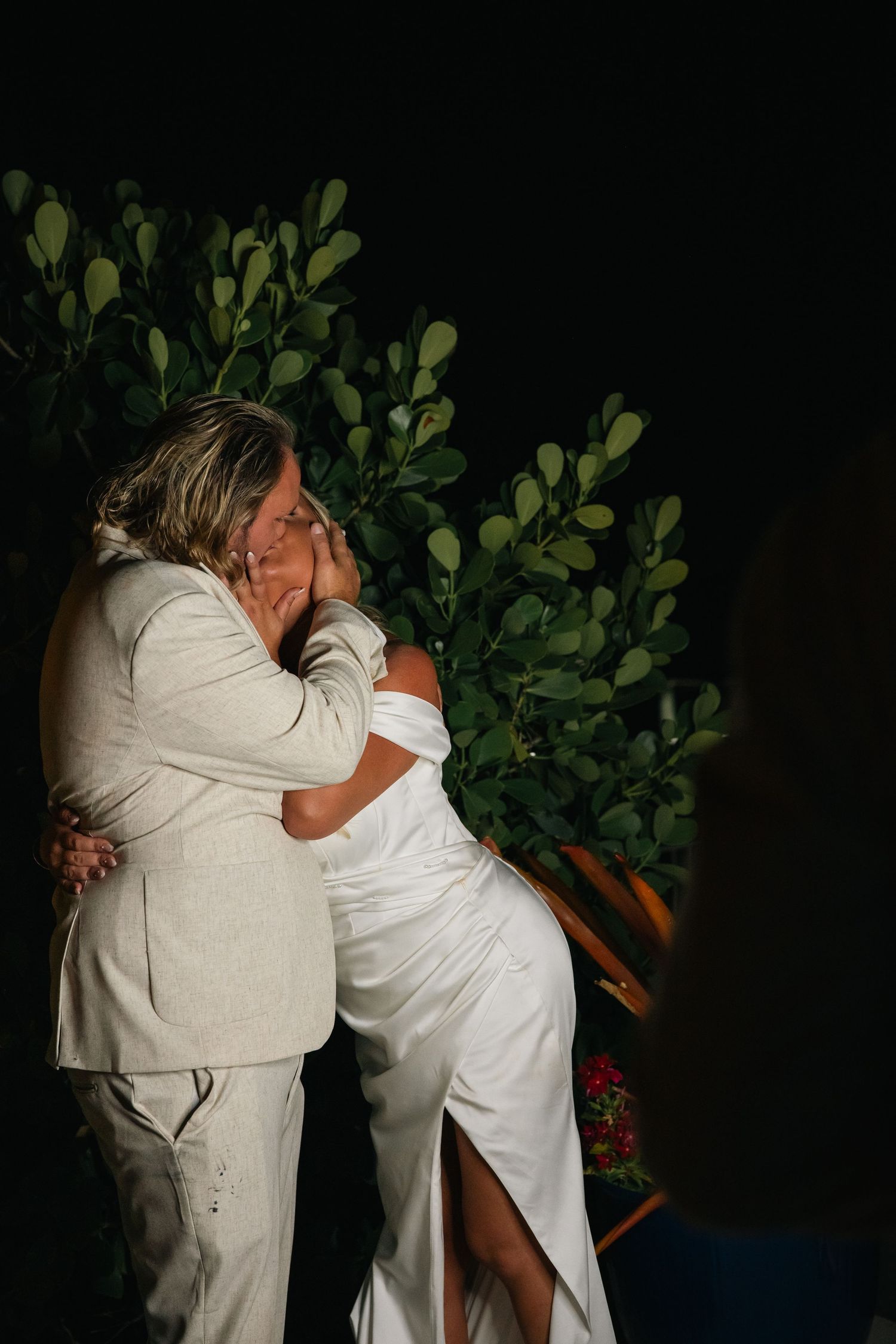Bride and groom share an emotional embrace during their wedding ceremony surrounded by lush greenery.