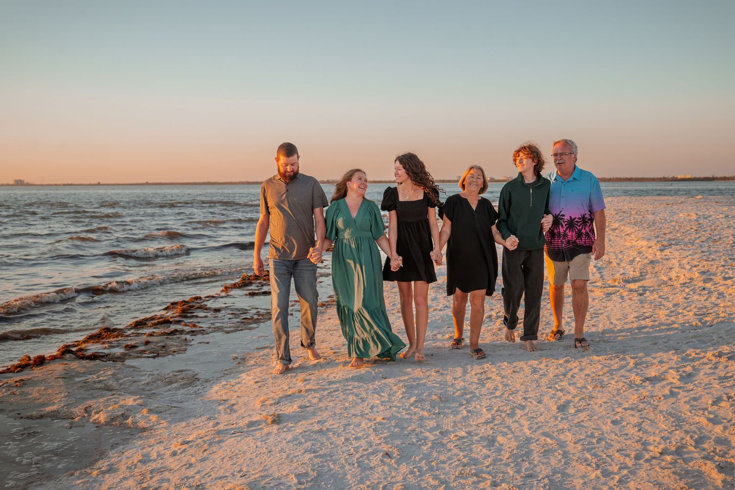 Six family members walk together along a white sand beach at sunset.