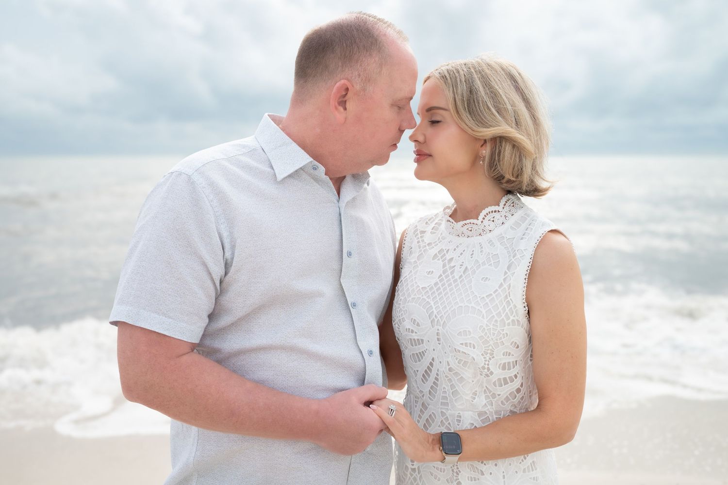 Romantic couple nearly kissing on beach with ocean waves in the background.