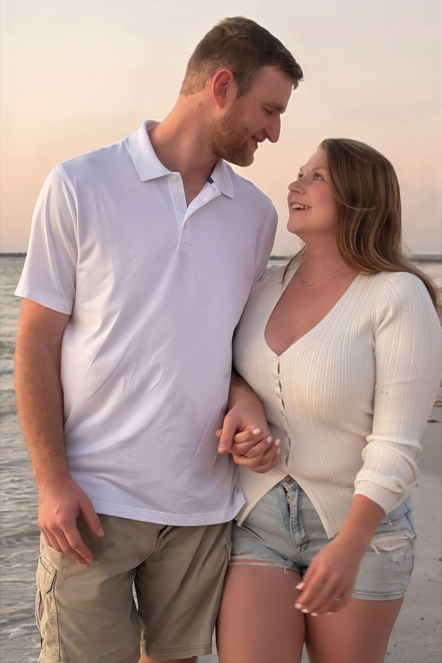 Happy couple holding hands and smiling at each other on a beautiful beach at sunset.