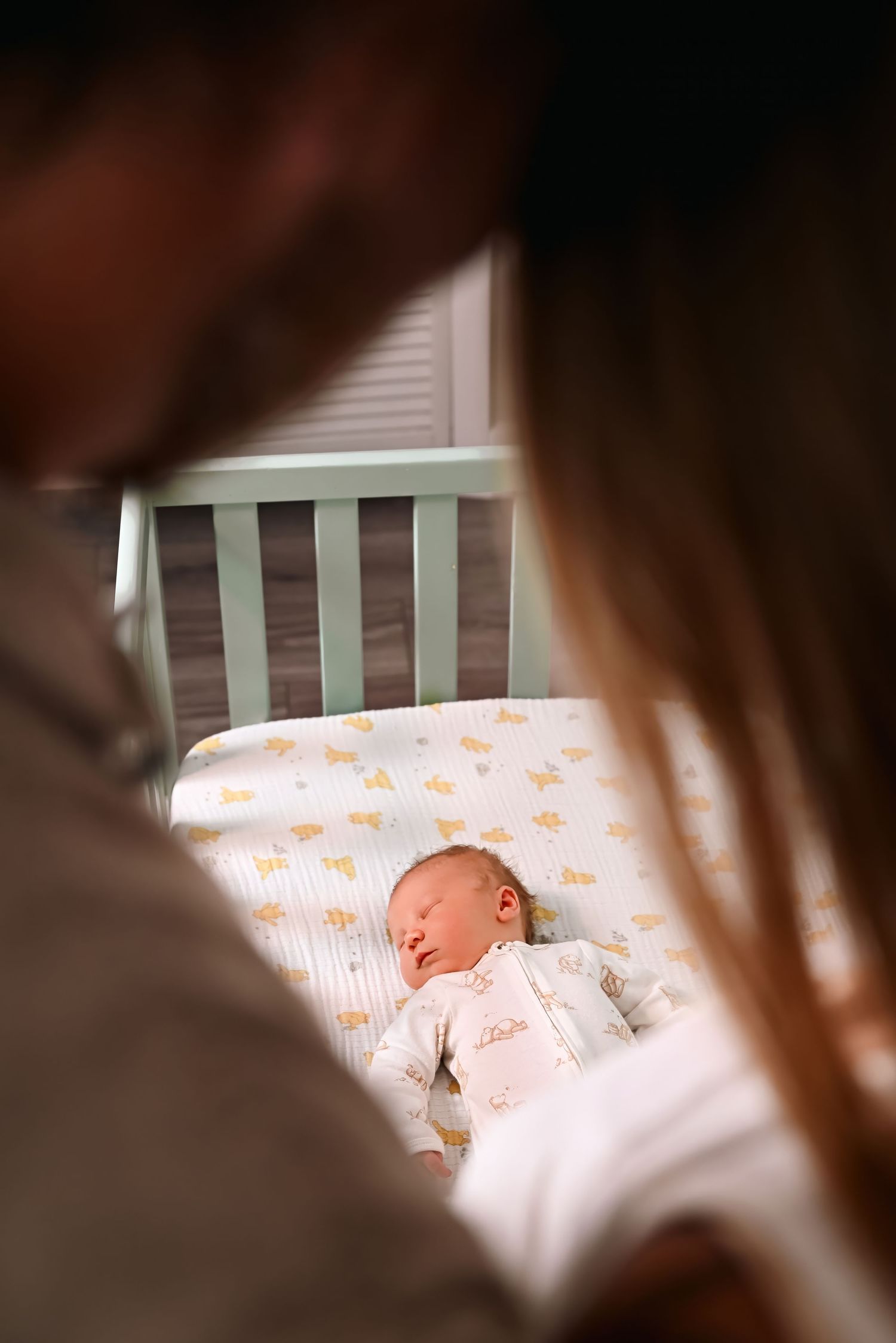 Two parents gazing lovingly at their sleeping newborn baby resting peacefully in a white crib.