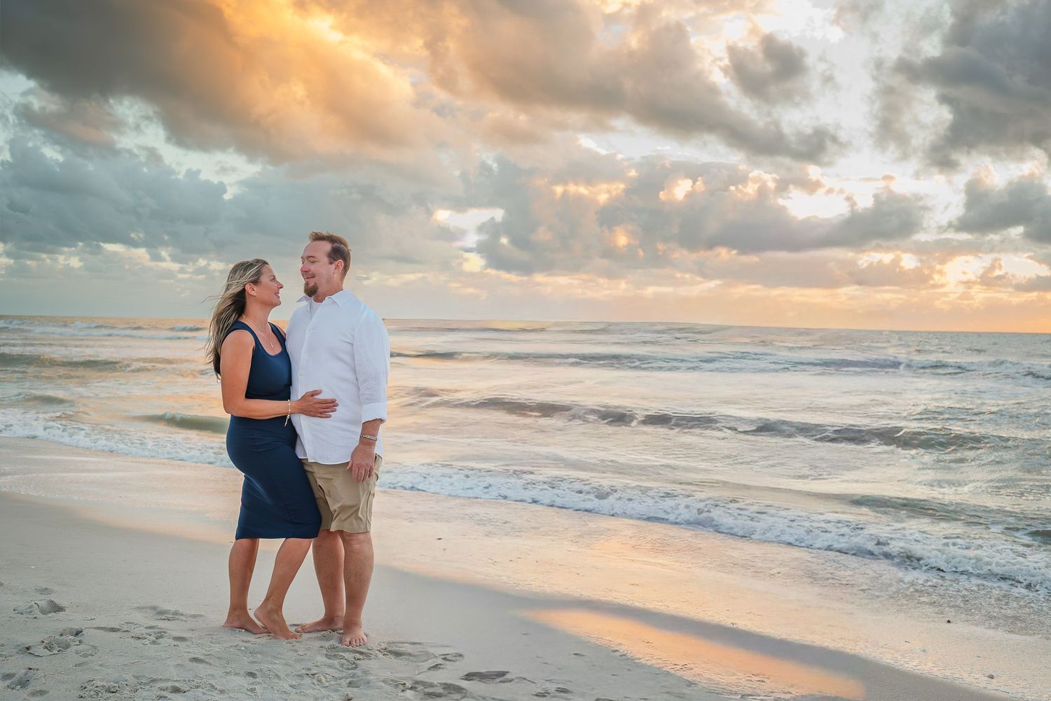 Couple standing close together on beach at dramatic golden sunset.