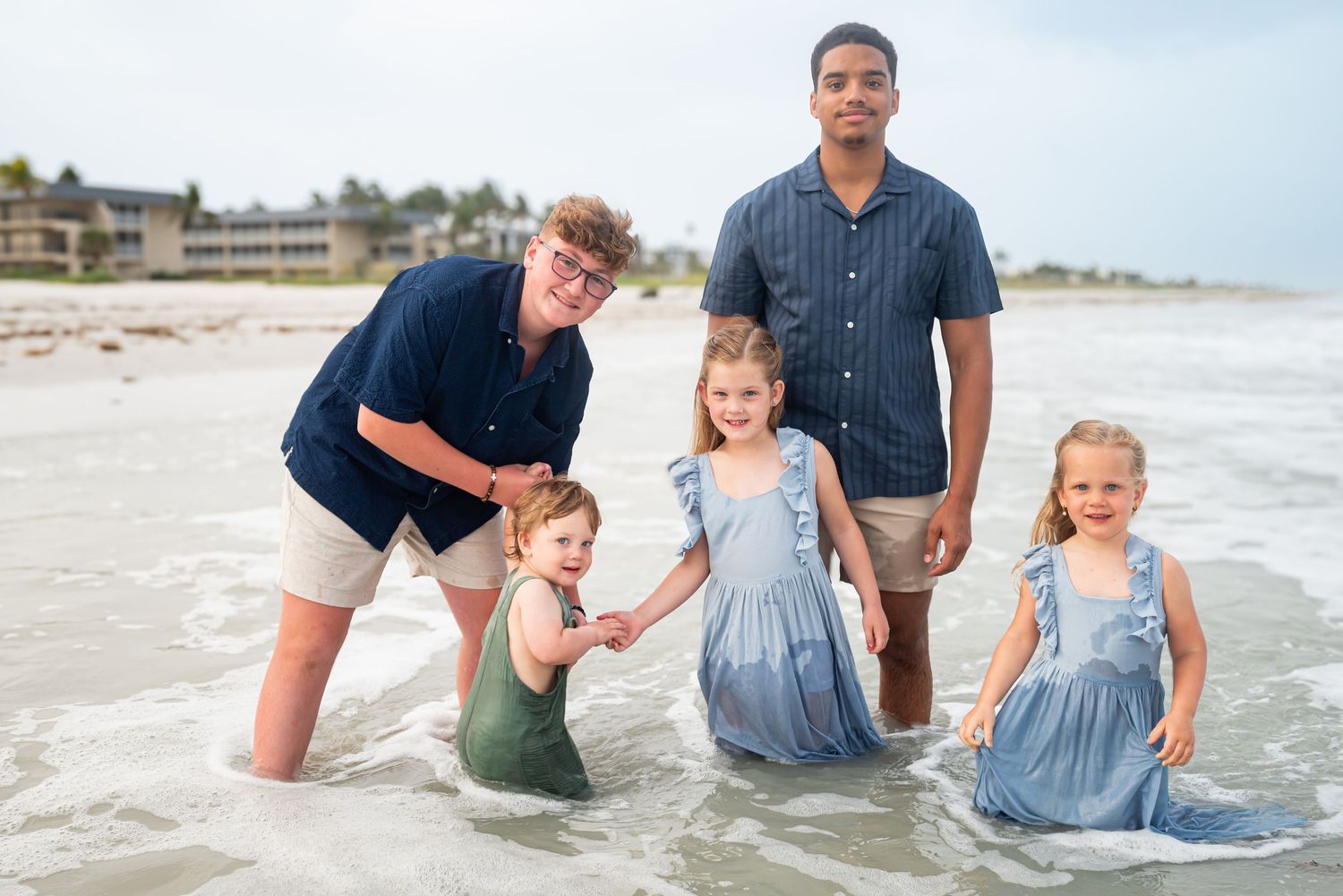 Two men pose with three young girls in blue dresses at the beach.