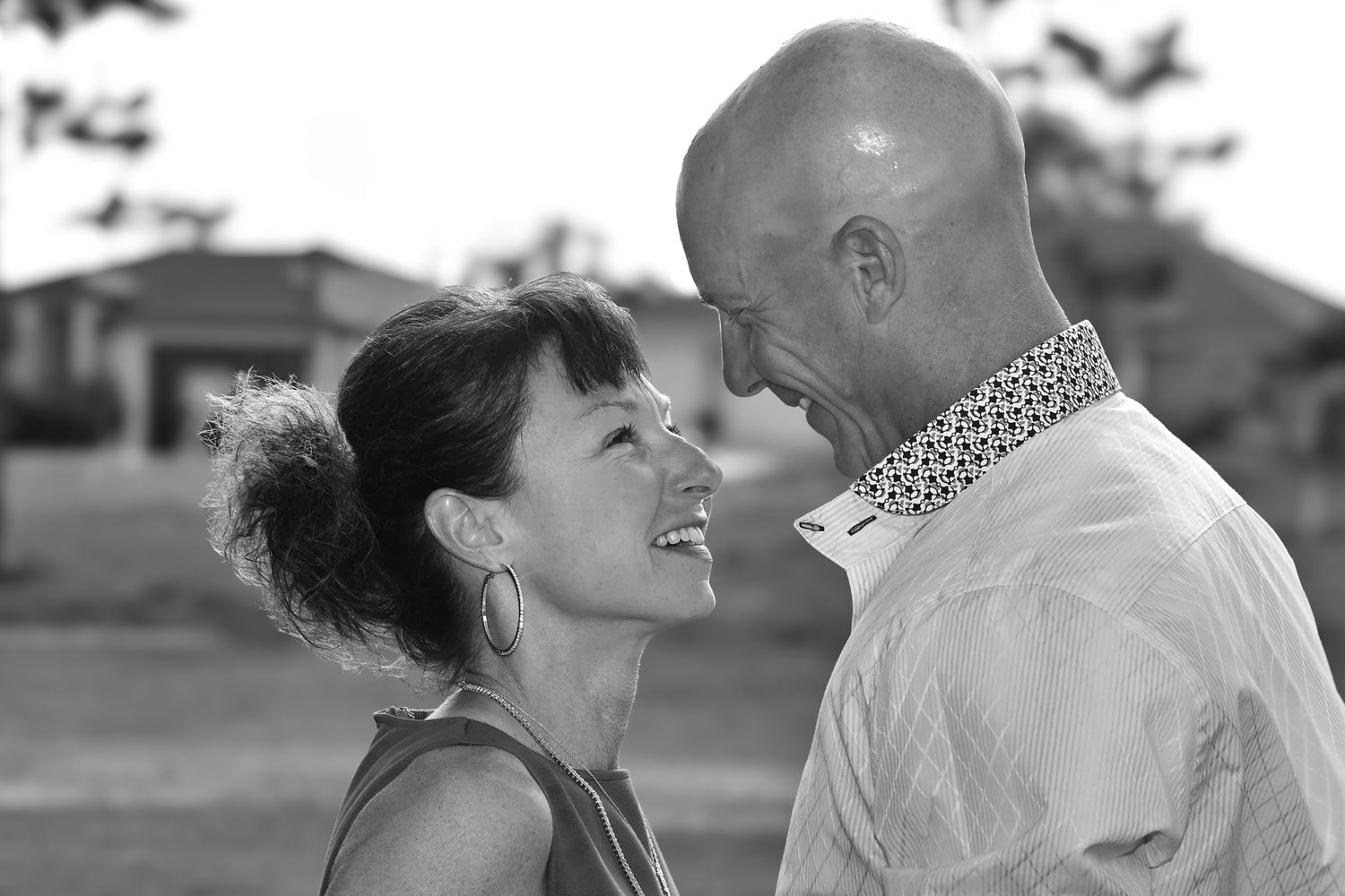 Black and white photo of laughing couple facing each other closely in outdoor setting.