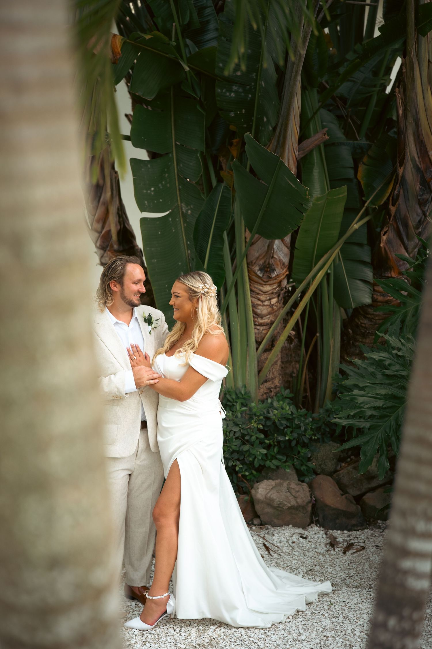 Bride and groom share a romantic moment surrounded by lush tropical greenery in a stunning outdoor wedding setting.