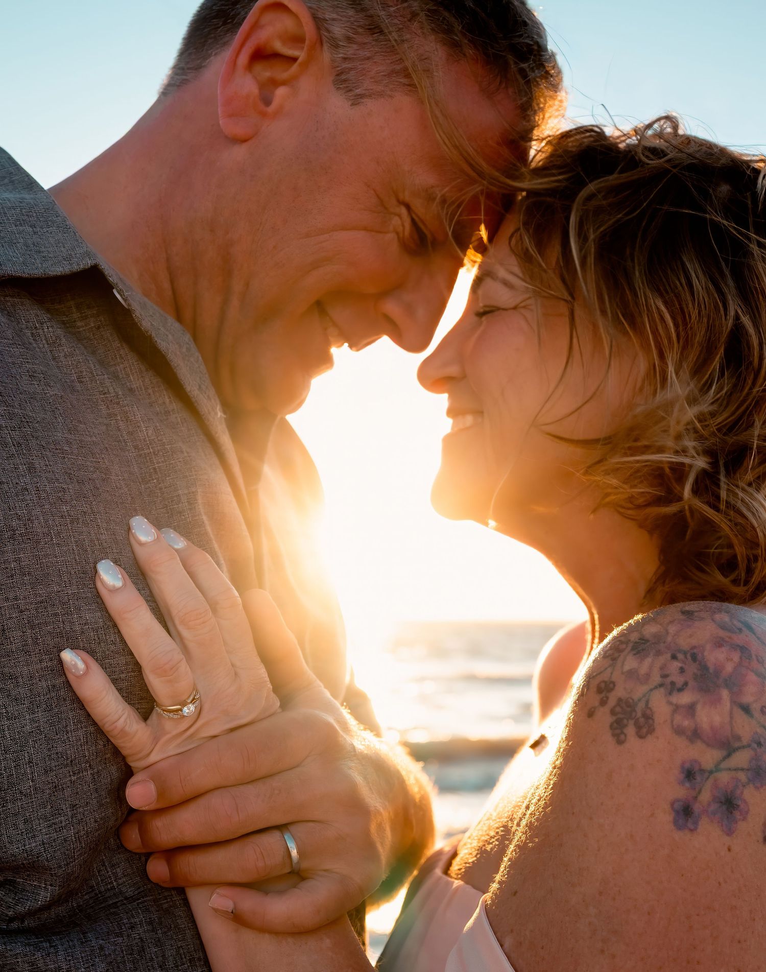Romantic couple touching foreheads in golden sunset light on the beach.