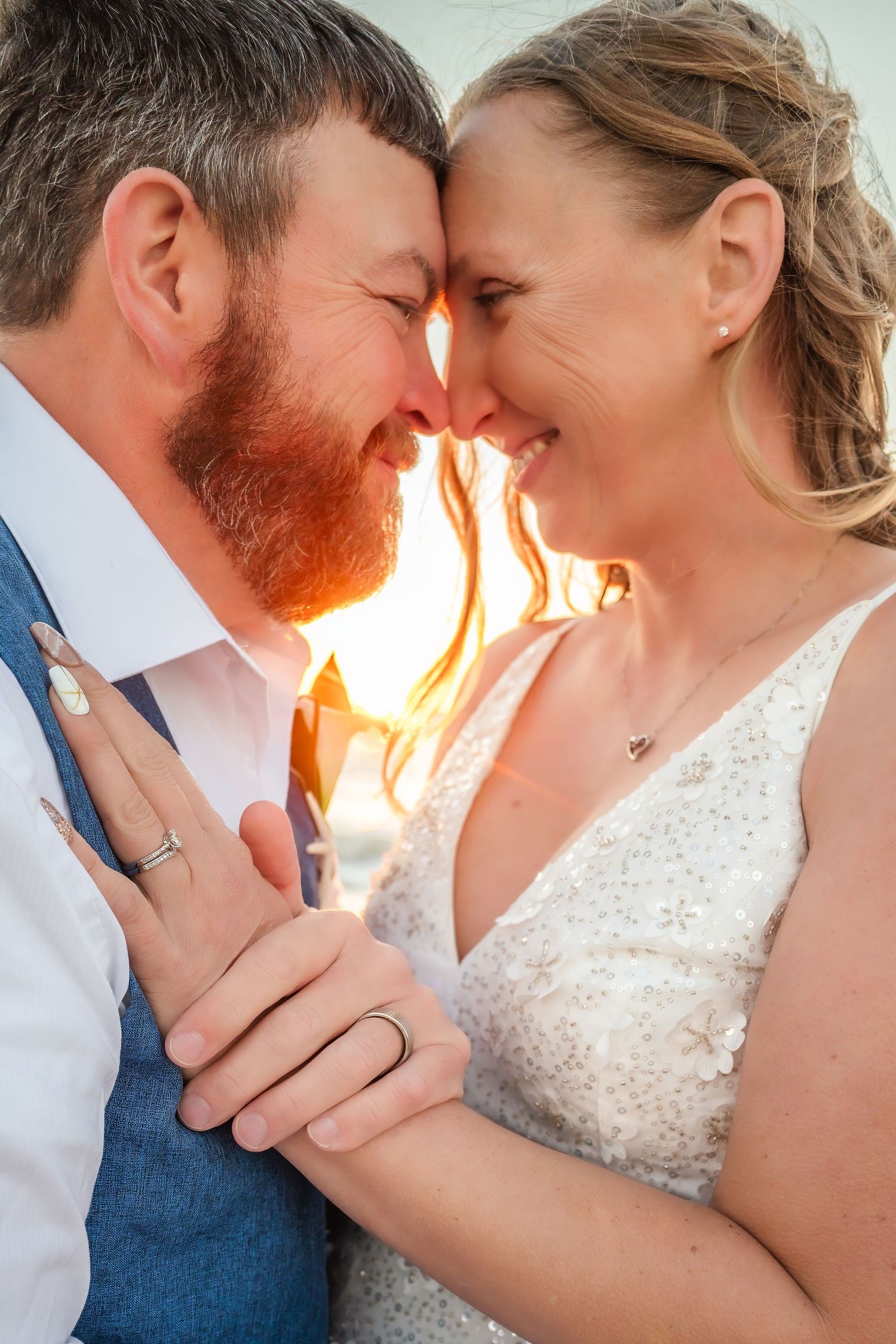 Romantic close-up of bride and groom touching foreheads at golden hour, both wearing wedding rings.