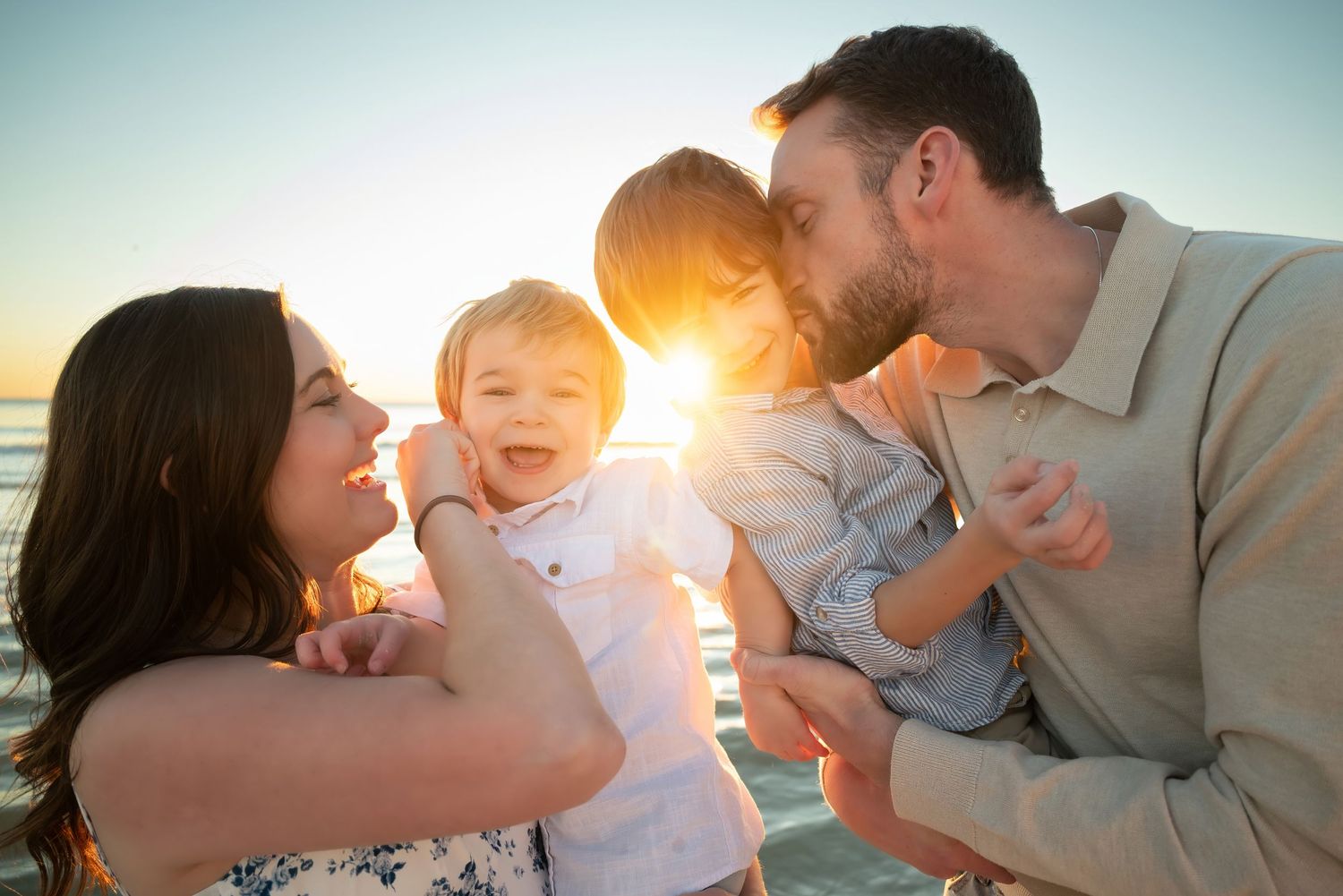 Happy family with two young children sharing kisses on sunny beach.