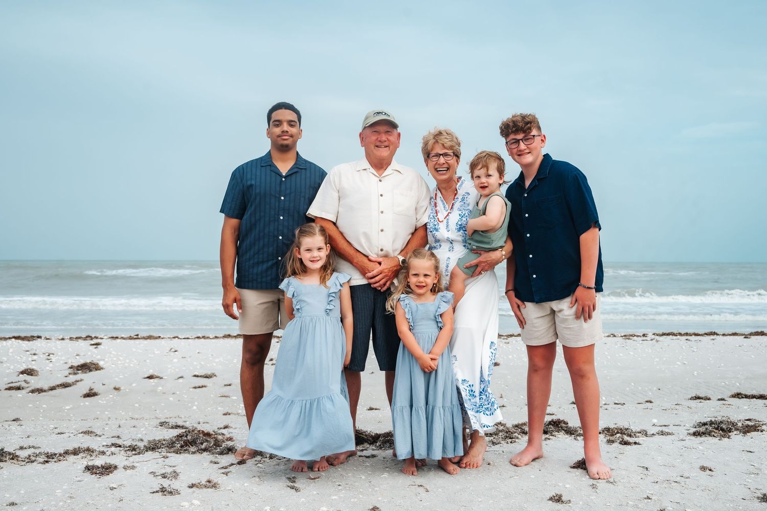 A multigenerational family of eight poses together on a beach.