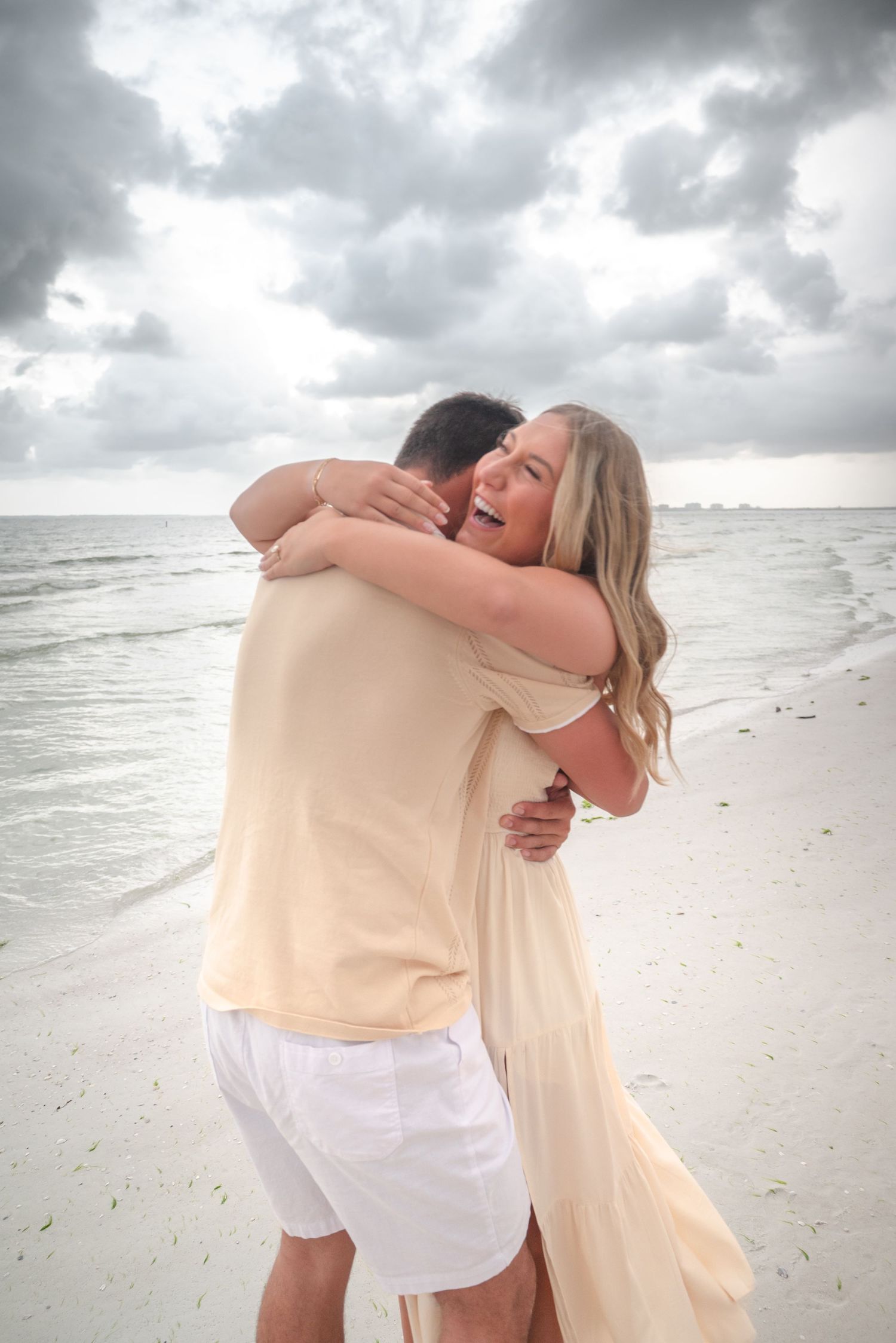 Joyful couple embracing and laughing on a sandy beach with ocean waves in the background.