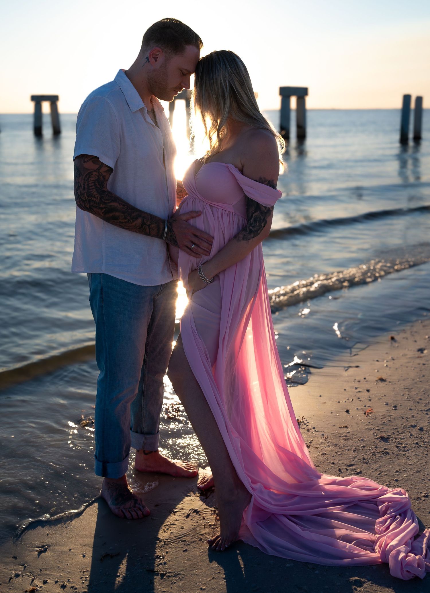 Expecting couple embracing on the beach at golden hour with a pink maternity gown.