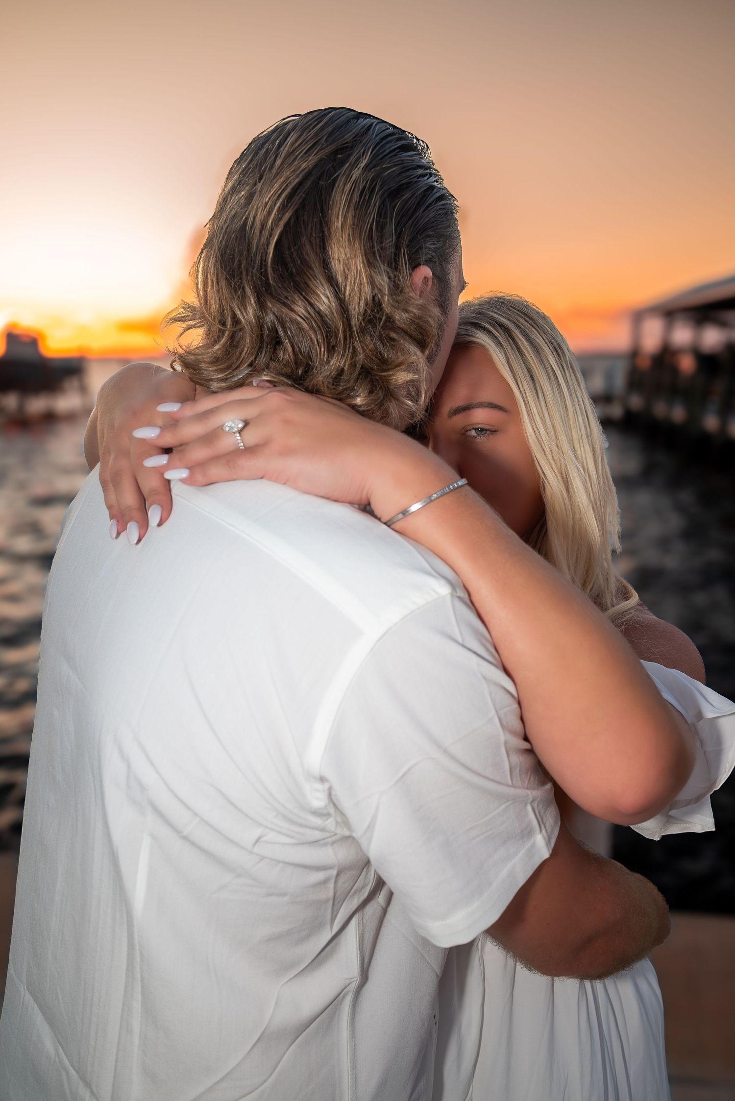 Newly engaged couple embracing at sunset, woman showing off her engagement ring.