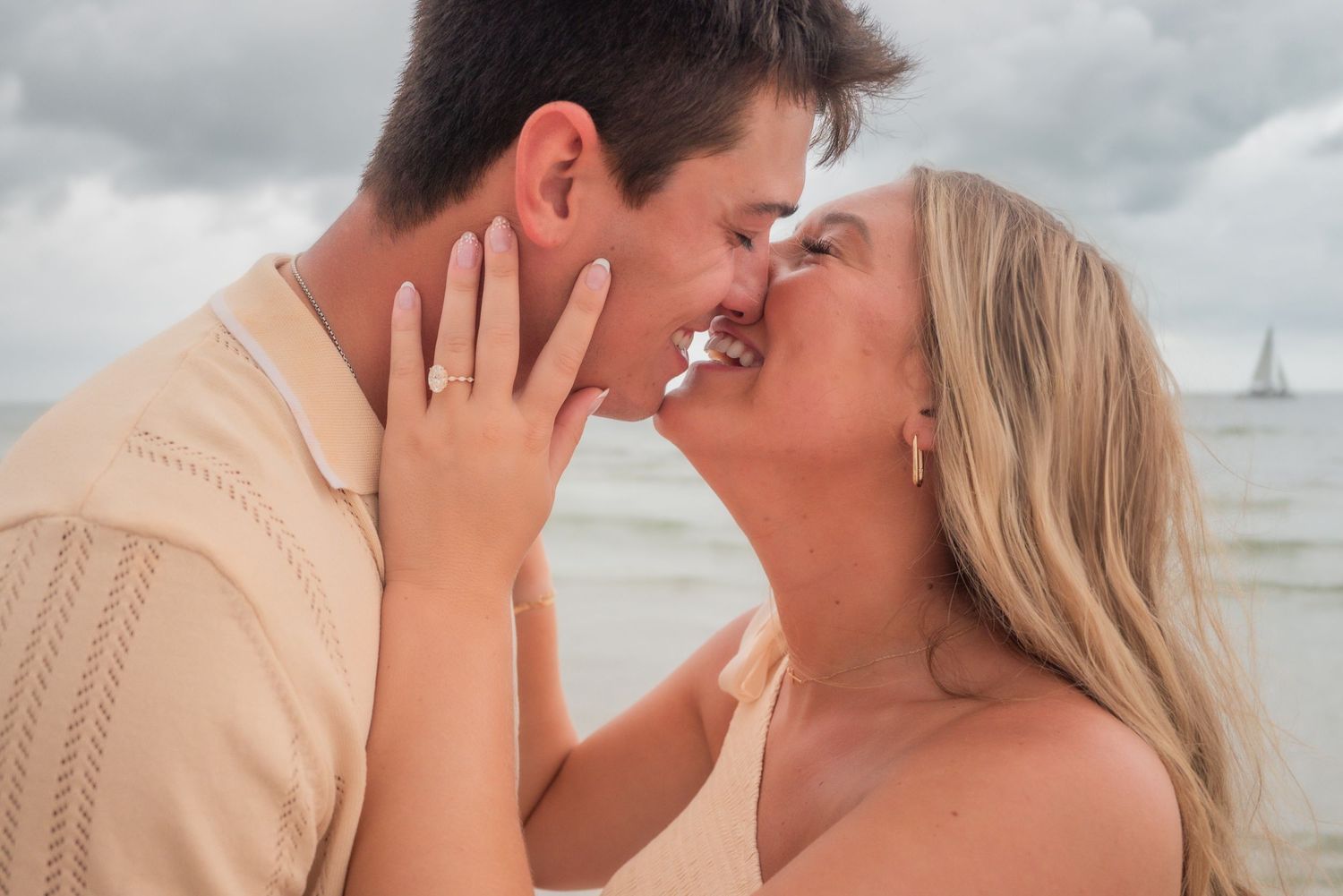 Newly engaged couple sharing a kiss on the beach, engagement ring visible on her hand.