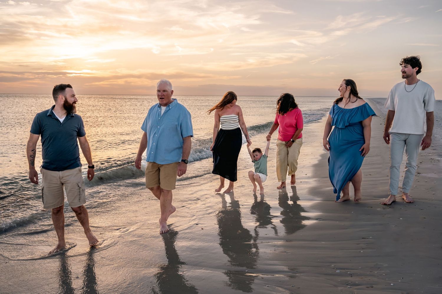 Multi-generational family walking together on a sandy beach at sunset, enjoying a peaceful seaside stroll.