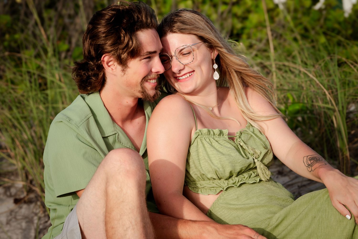 Happy young couple in green outfits sitting together outdoors, smiling and sharing a romantic moment.