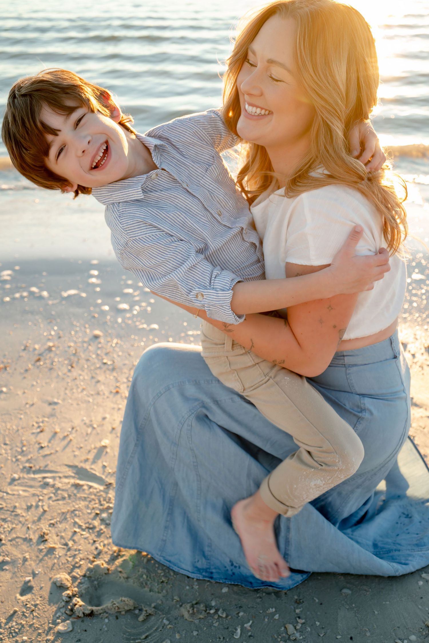 Mom hugging laughing child on sunny beach at golden hour.