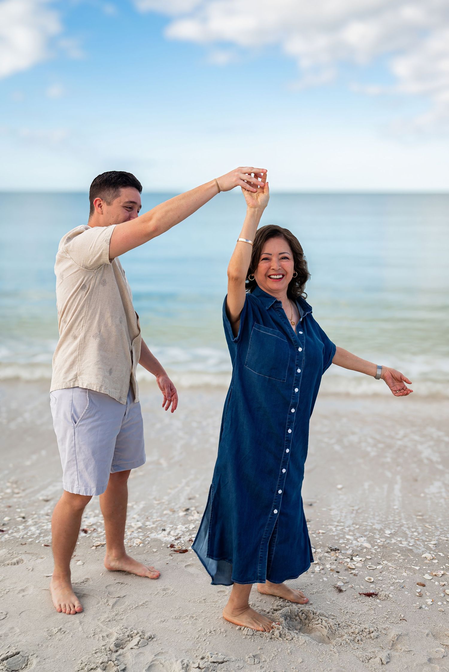Man spinning woman in blue dress on a sunny beach by the ocean.