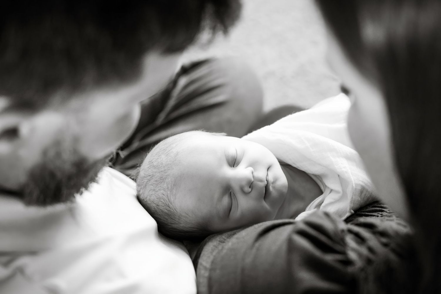 Black and white photo of a newborn baby sleeping peacefully in a bearded fathers arms.