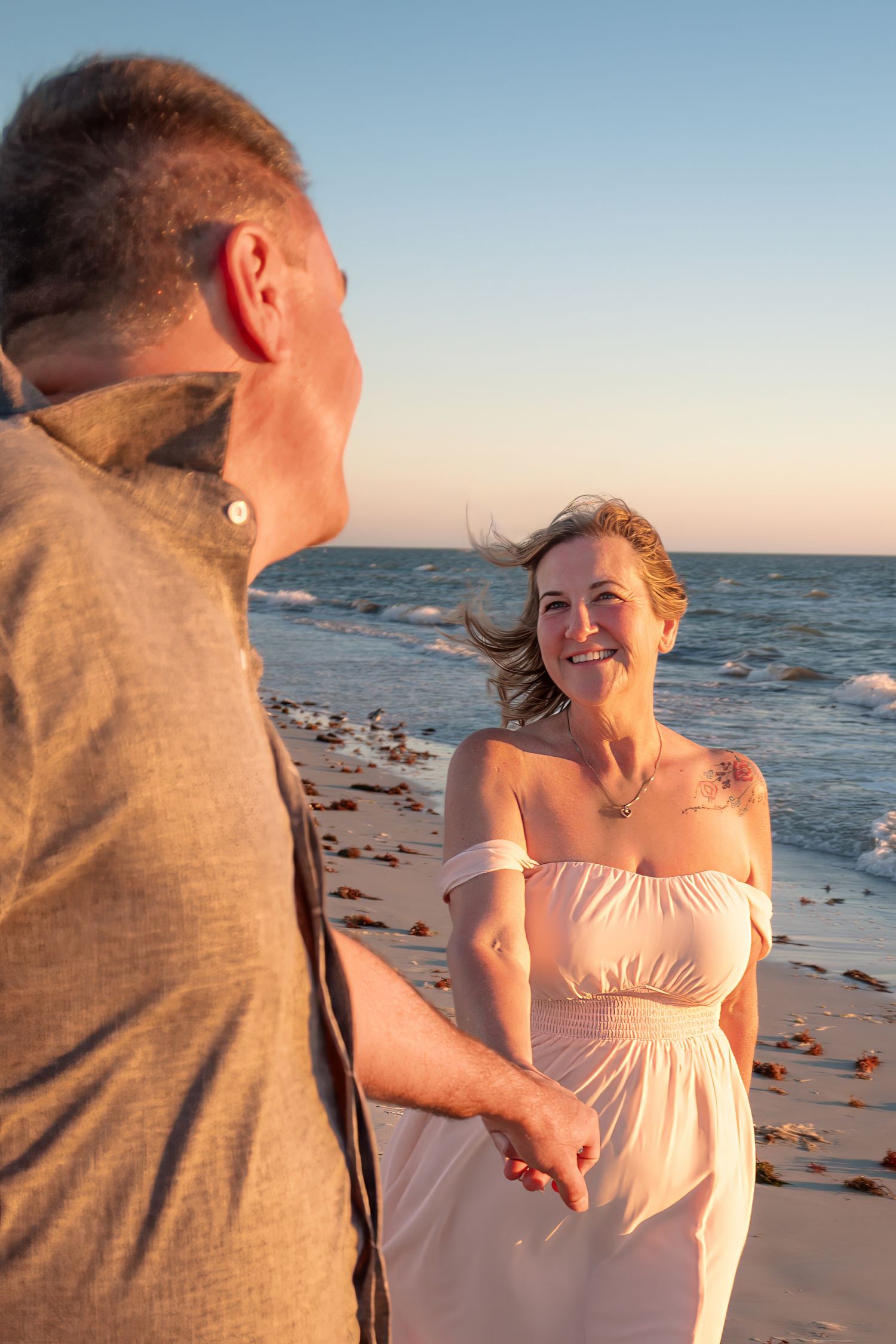 Smiling woman holds hands with a man on a rocky beach during golden hour.
